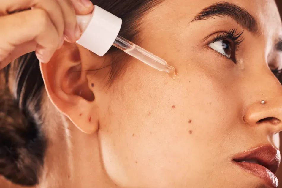 Un gotero aplica sérum en la mejilla de una mujer en una rutina de cuidado facial en primer plano.