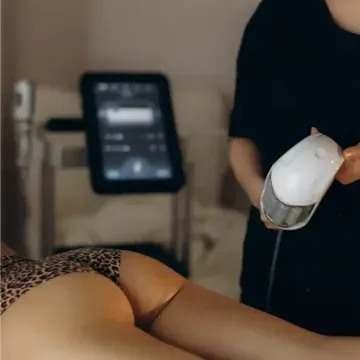 Persona que utiliza un dispositivo de masaje manual sobre un cliente recostado en una sala de spa.