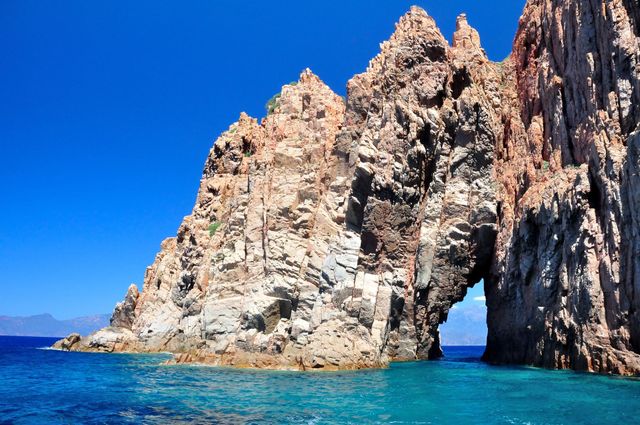 Arche rocheuse sur une côte, eau bleue, ciel clair.