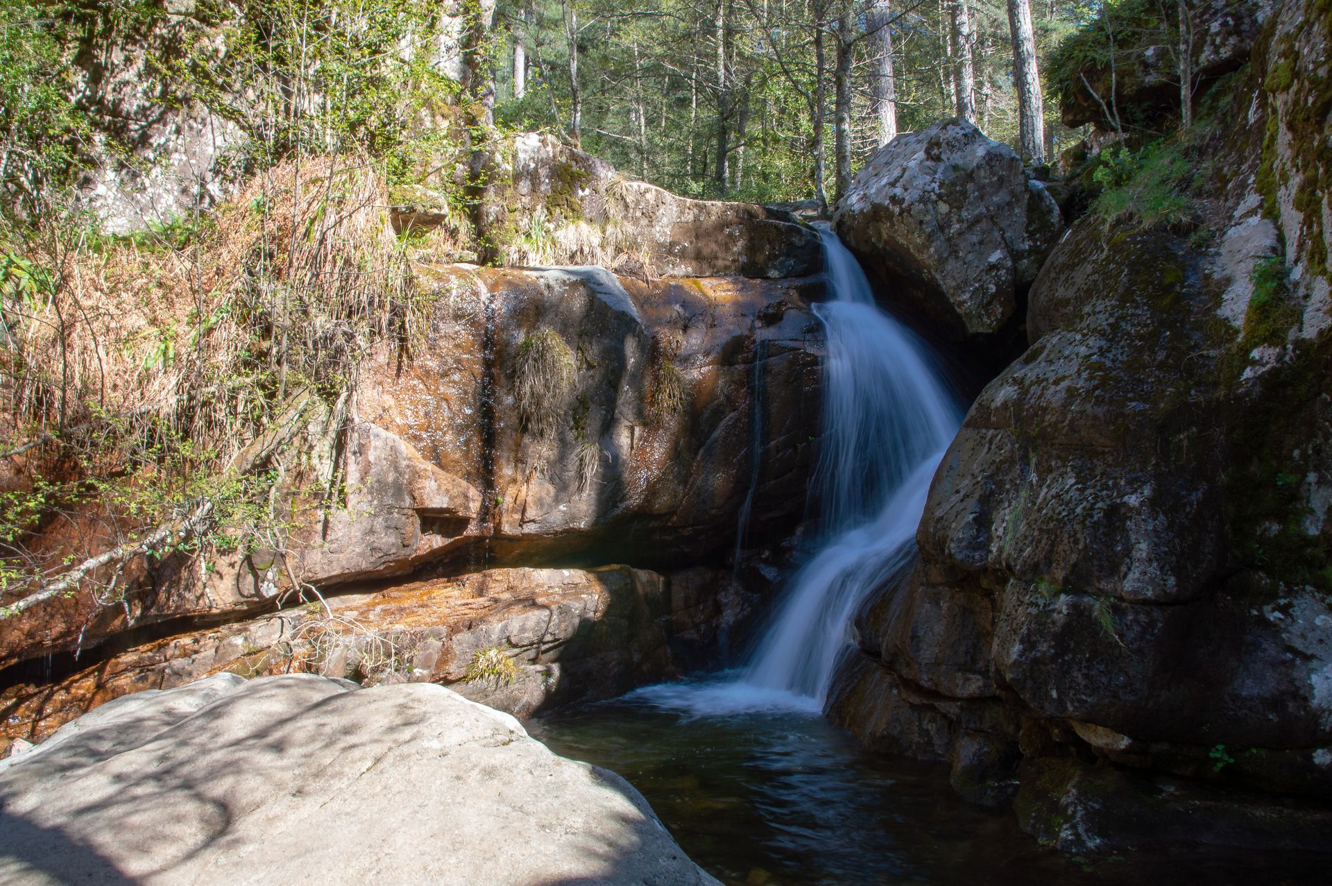 Cascade tombant dans une piscine naturelle entourée de gros rochers et de forêt.