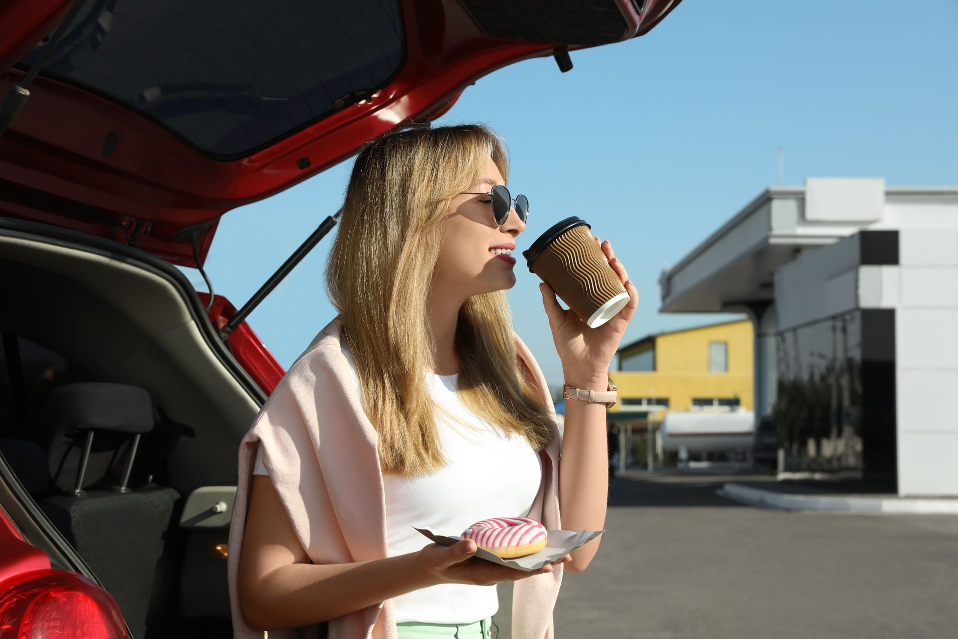 Femme qui boit un café derrière sa voiture