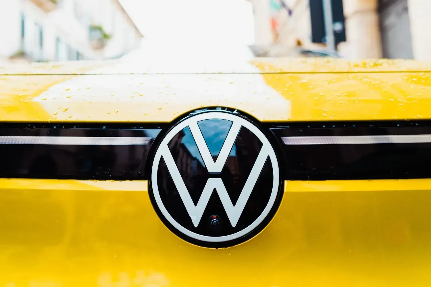 Primer plano del logotipo circular de Volkswagen en la parte delantera de un vehículo amarillo brillante.