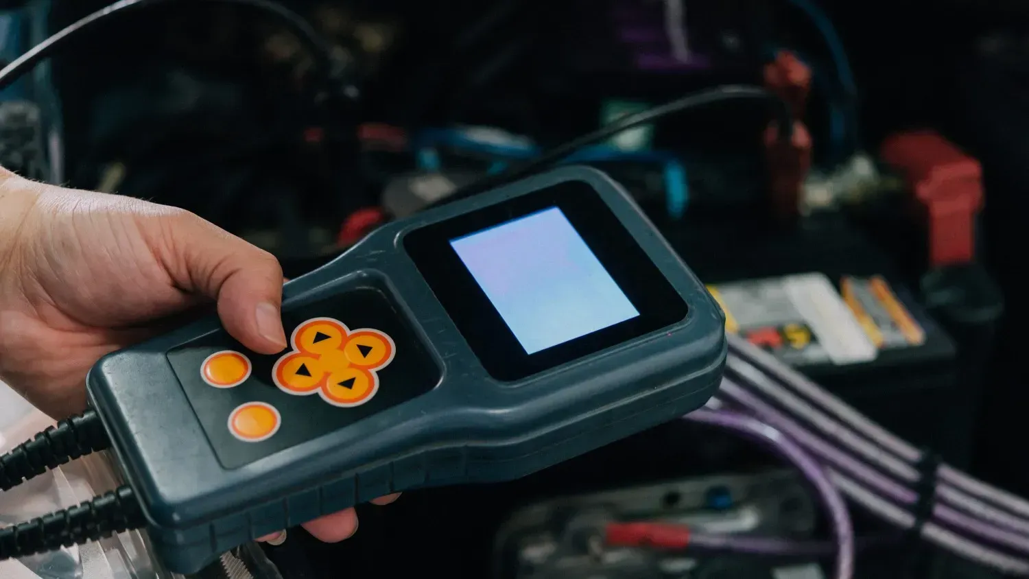 Una mano sostiene un escáner de diagnóstico gris con pantalla y botones naranjas..