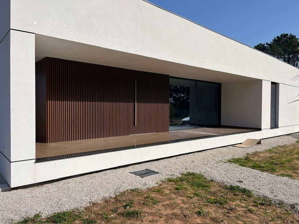 Maison blanche moderne avec porche couvert, claustra en bois et allée de gravier