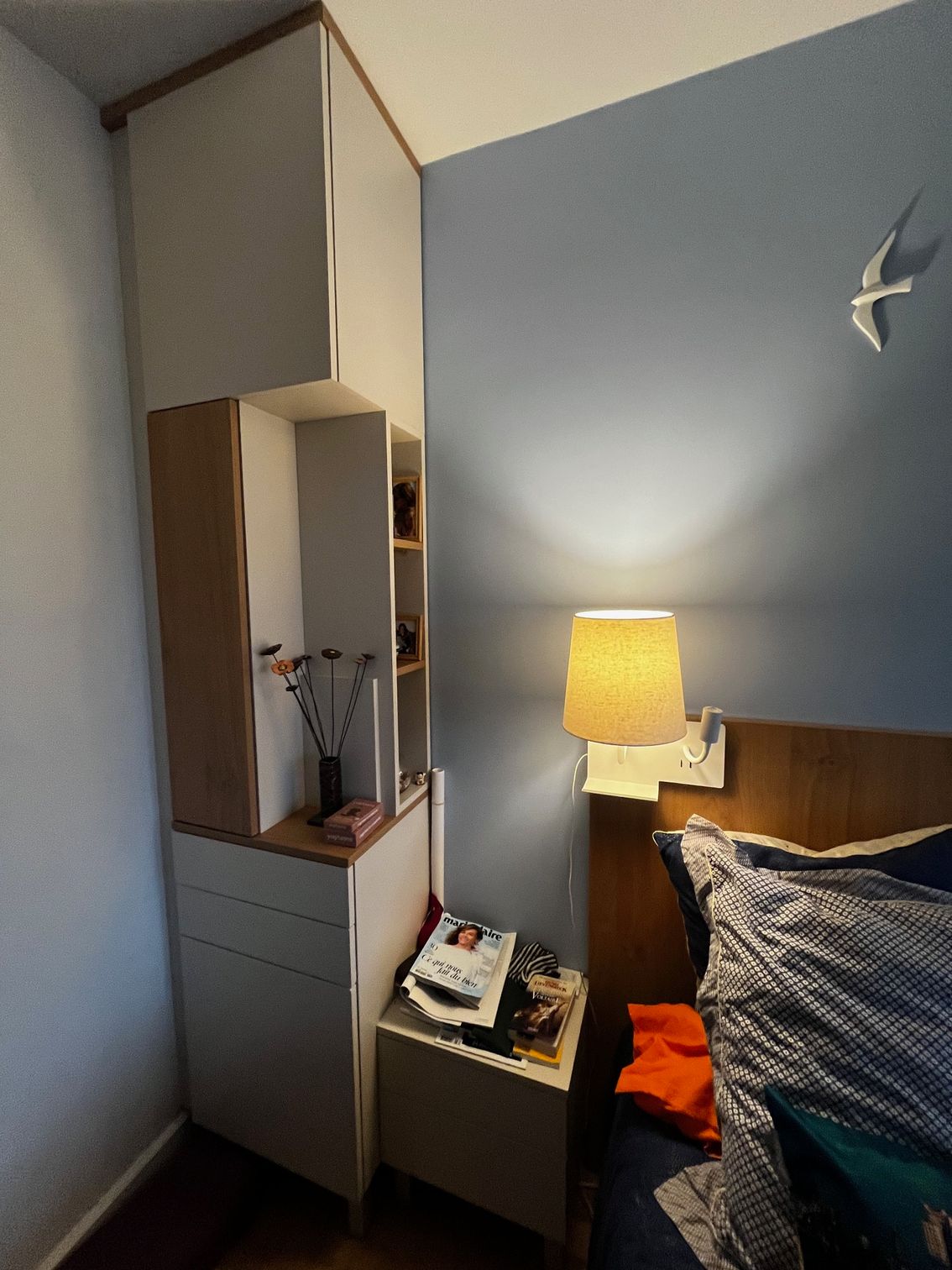 Petite chambre aux murs bleus, lampe de chevet, lit et armoire haute.