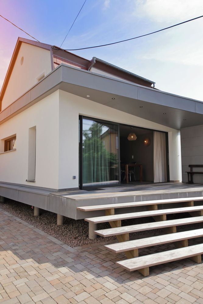Maison blanche moderne avec de grandes portes vitrées, des marches extérieures et une terrasse surélevée