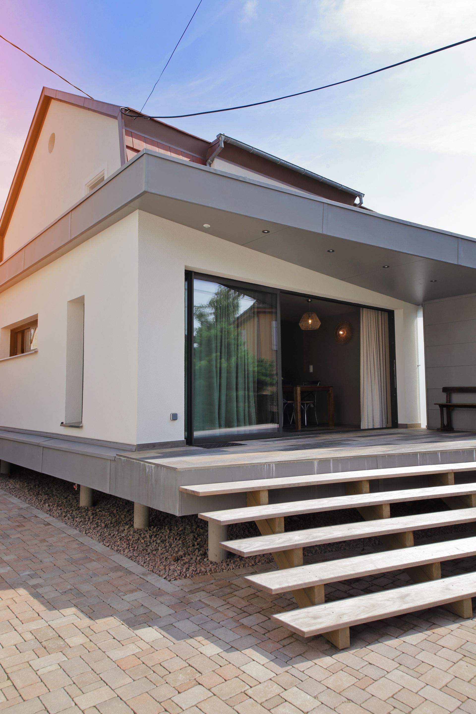 Maison blanche moderne avec de grandes portes vitrées, des marches extérieures et une terrasse surélevée