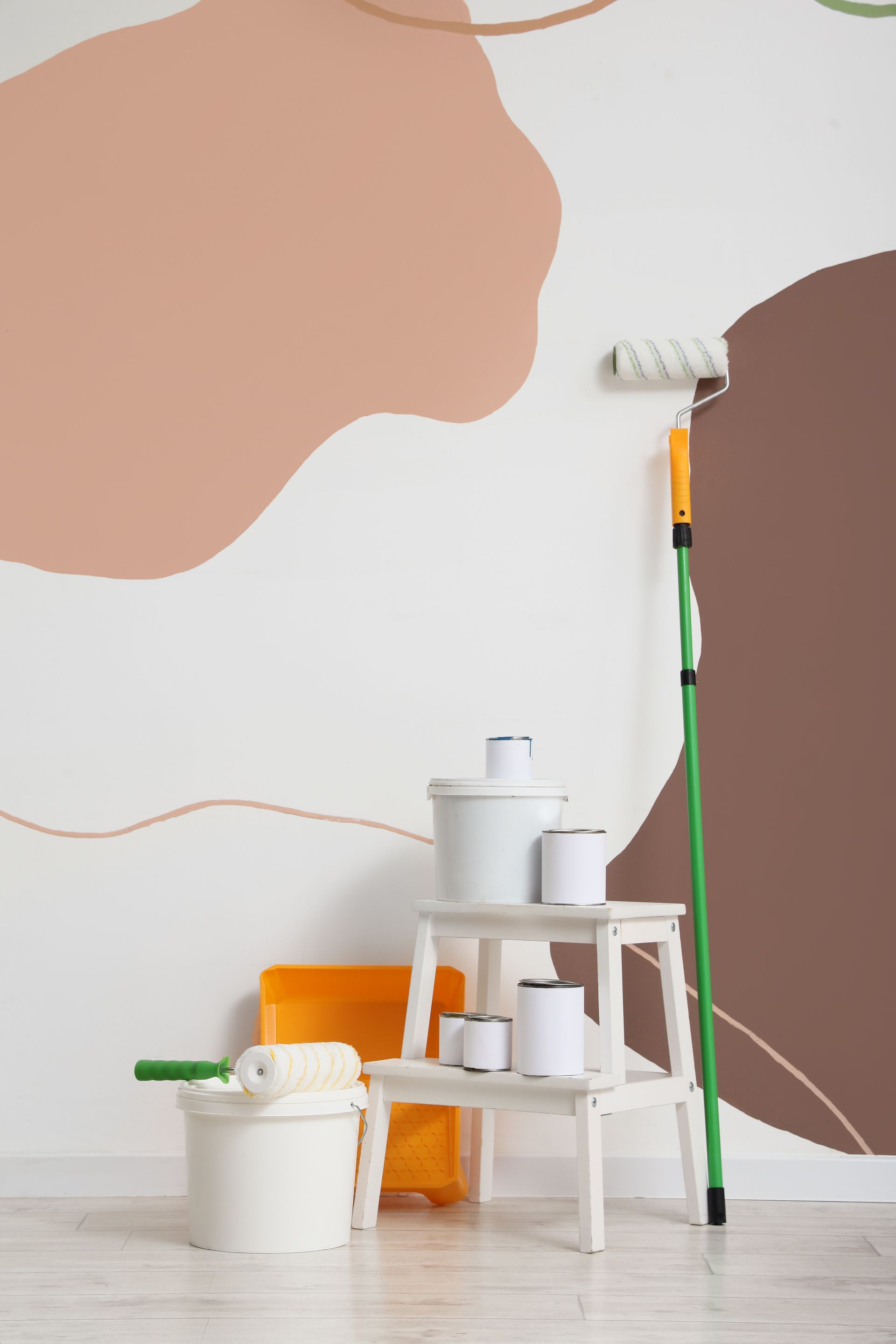 Matériel de peinture disposé à côté d'un mur orné de formes abstraites beiges et brunes, notamment un rouleau