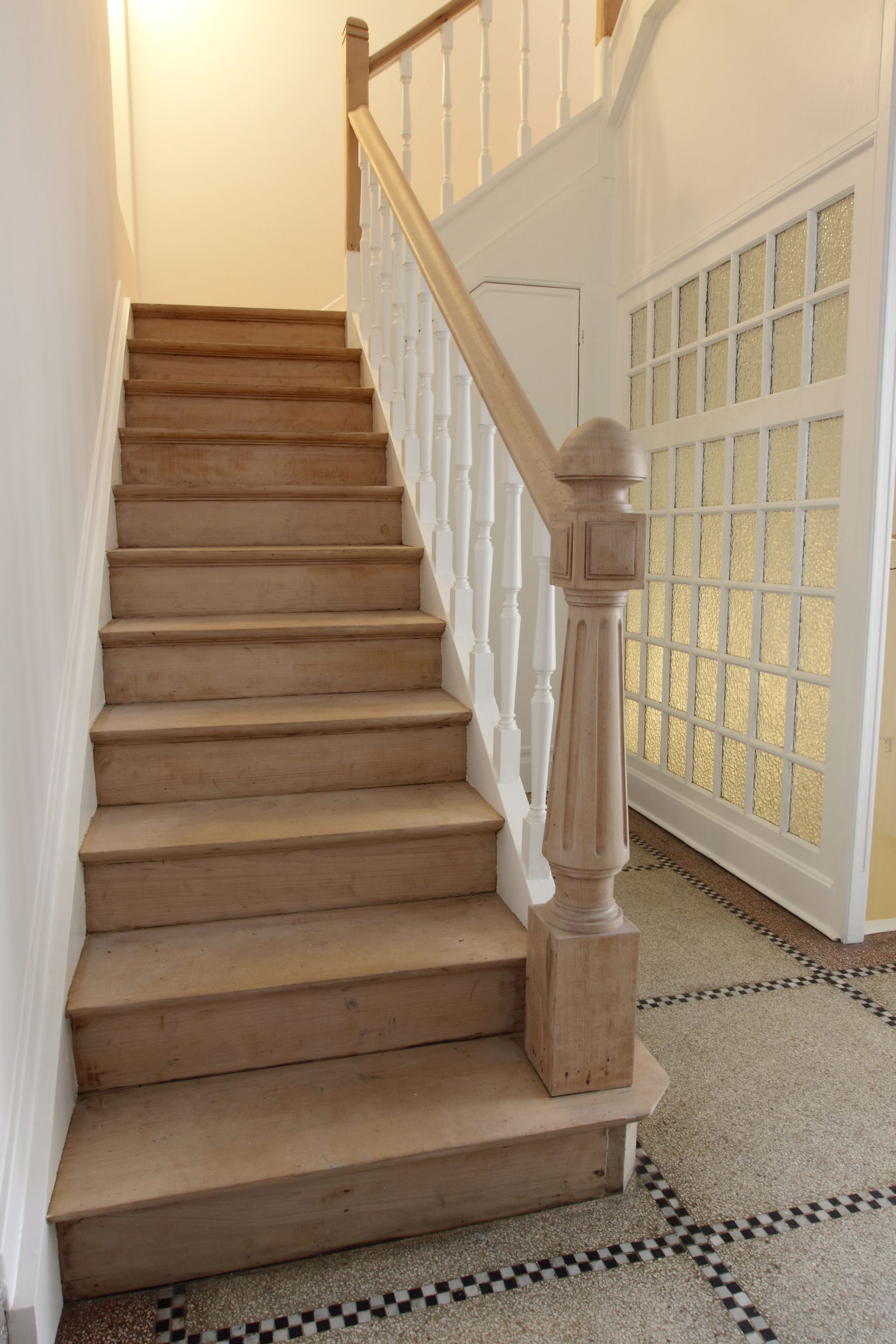 Escalier intérieur avec moquette beige, rampe blanche et sol carrelé à motifs à côté.