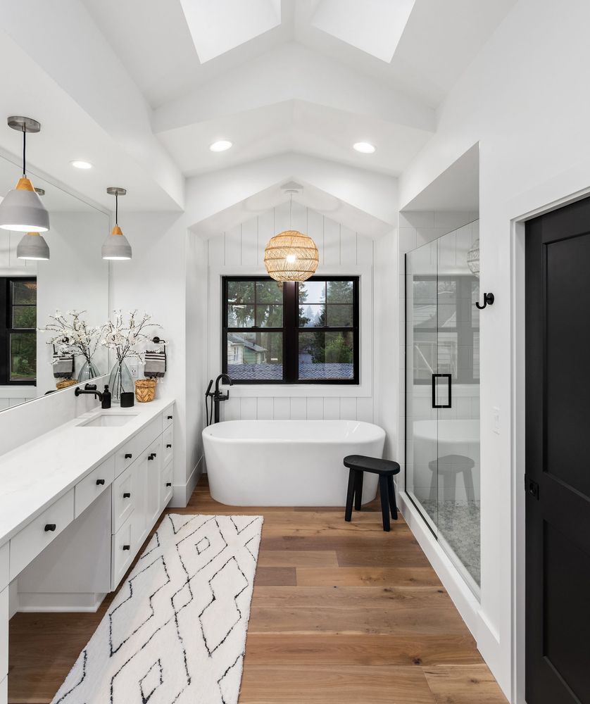 Salle de bains moderne et lumineuse avec baignoire îlot, meuble-lavabo blanc, douche en verre et parquet.