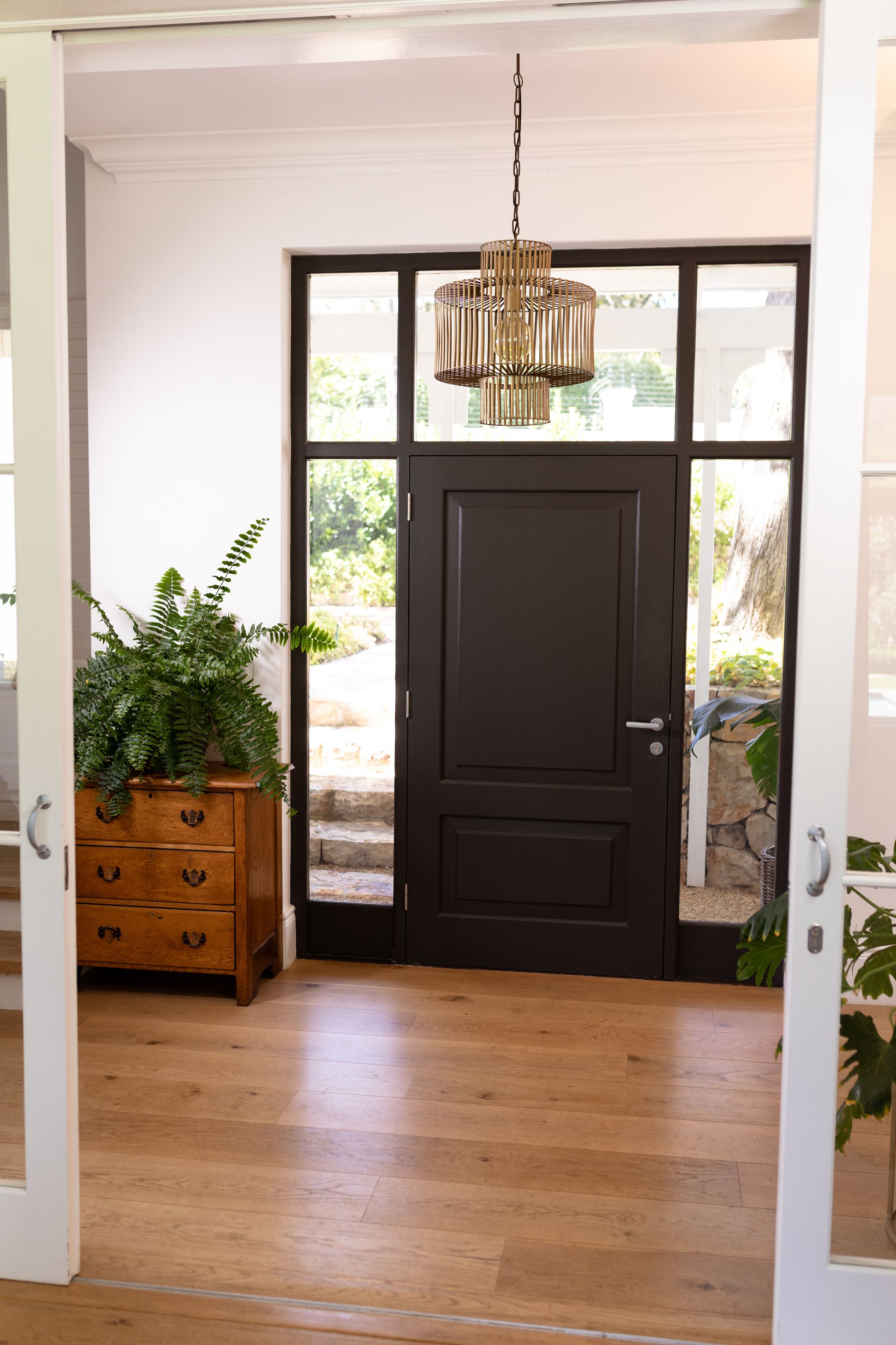 Entrée lumineuse avec porte d'entrée noire, parquet et lustre suspendu.