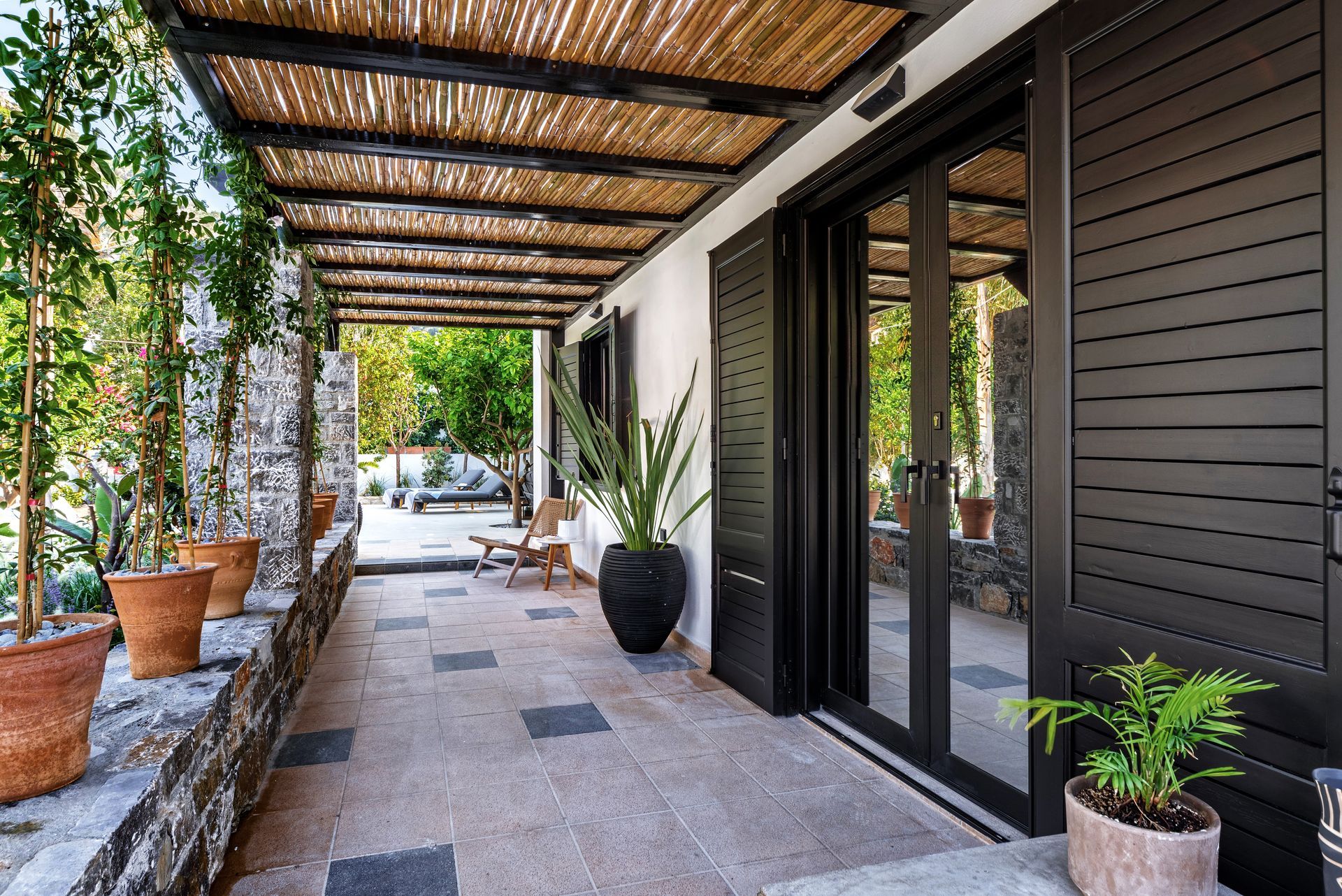 Allée couverte avec plantes en pot, sol en pierre et portes coulissantes en verre.
