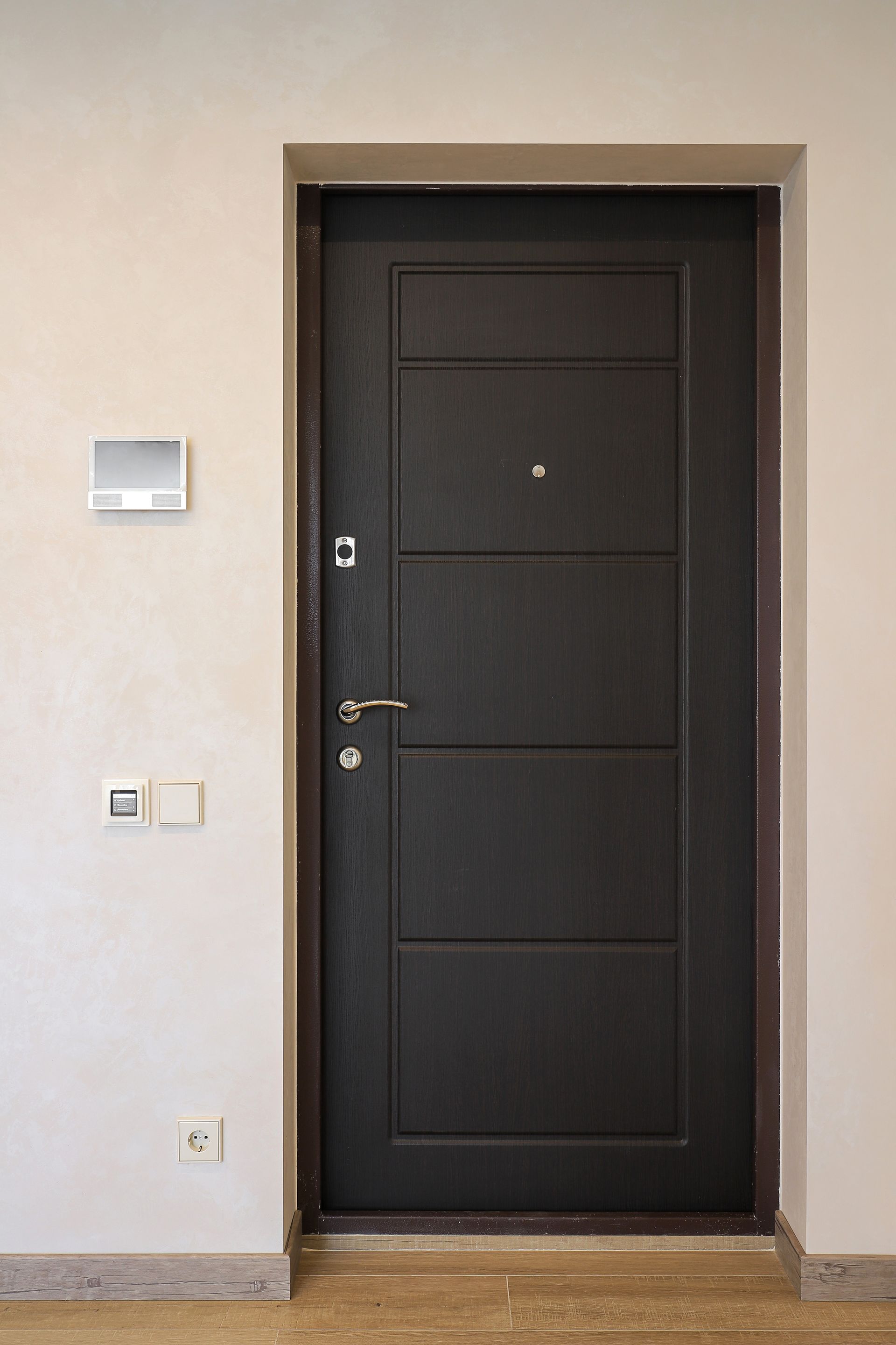 Porte d'entrée noire avec poignée argentée dans un couloir beige.