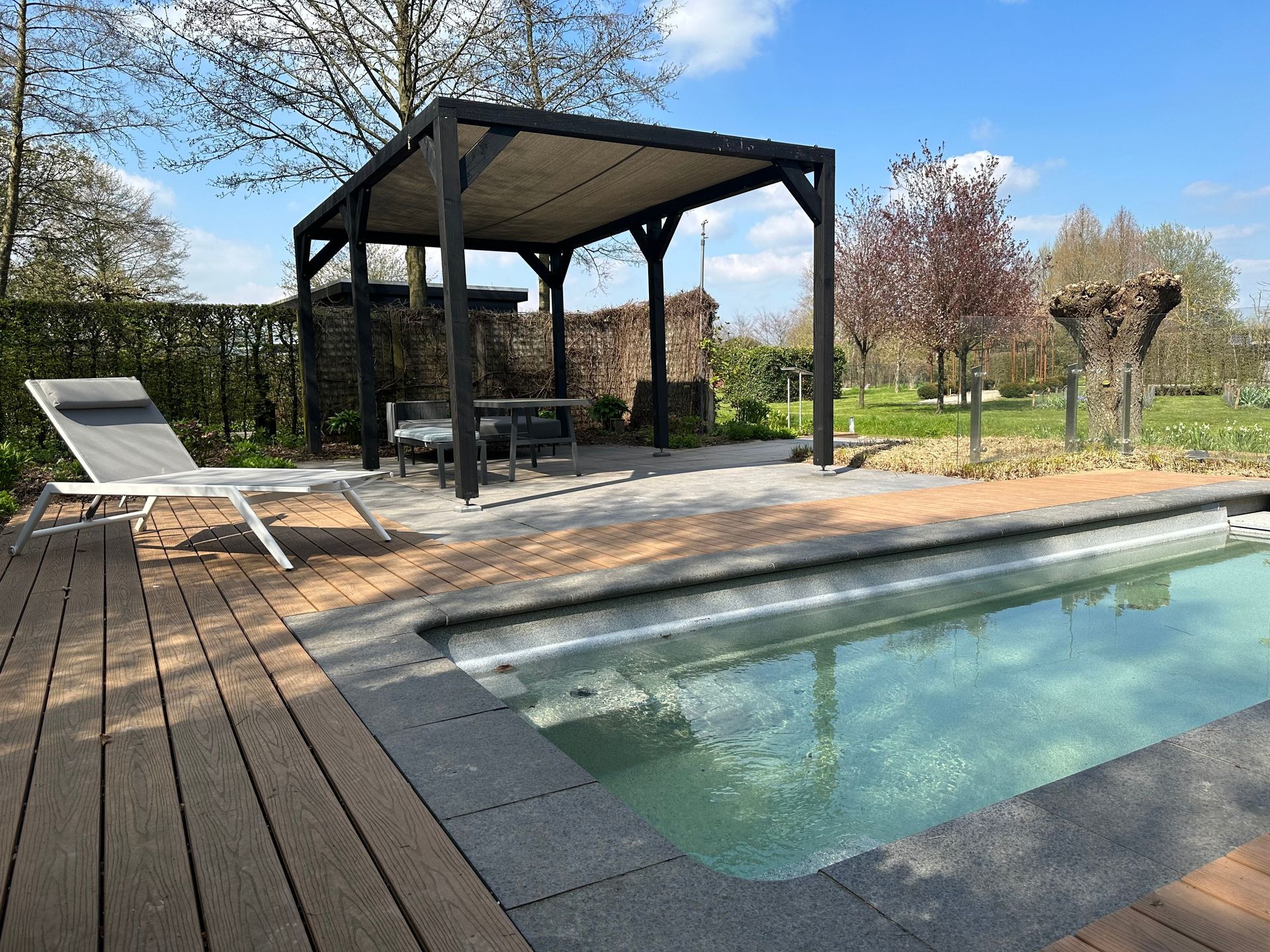 Piscine dans le jardin à côté d'un gazebo noir et d'une chaise longue sur une terrasse en bois