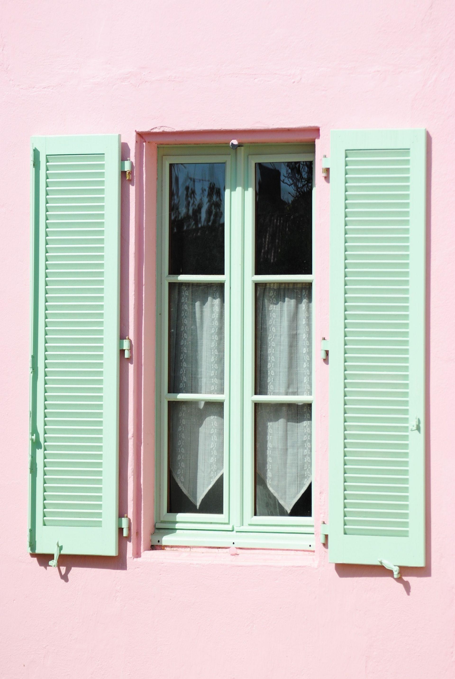 Volets vert menthe sur une fenêtre à cadre blanc, le tout sur un mur rose