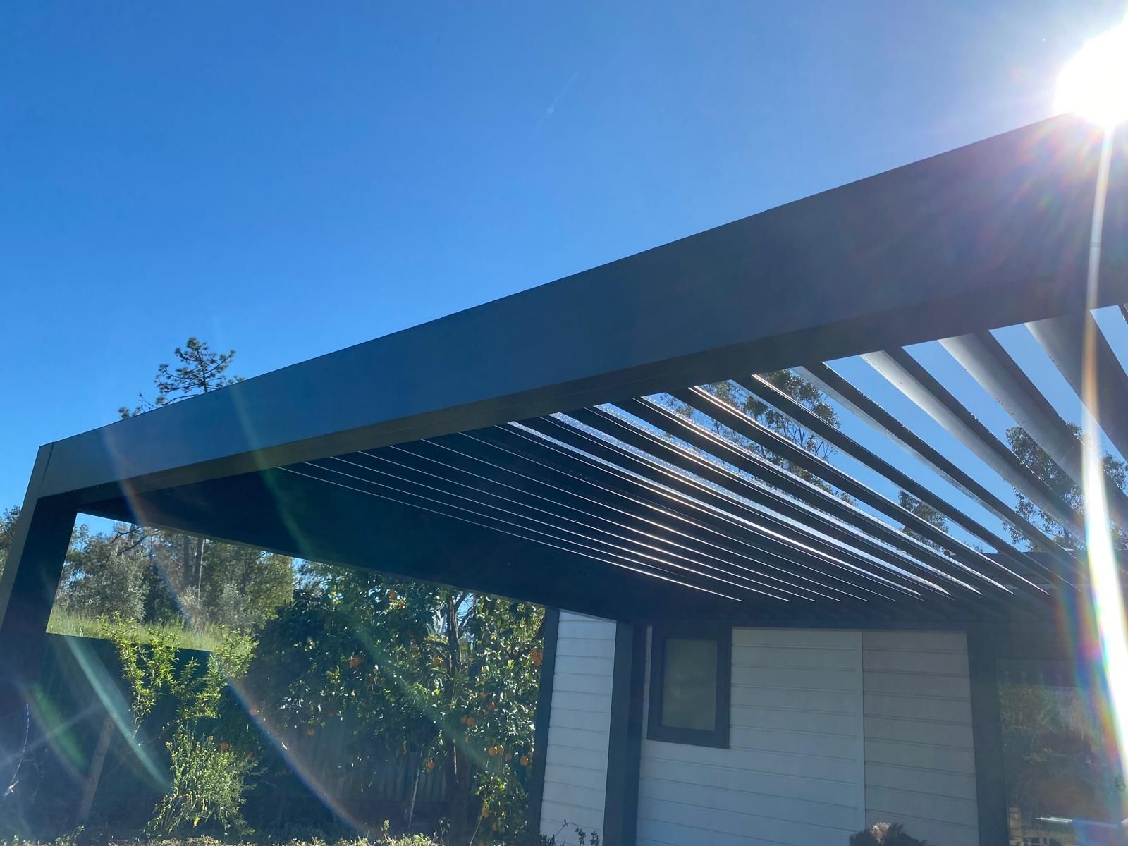 Extérieur de maison moderne avec toit en pergola sombre et reflets lumineux du soleil dans un ciel bleu