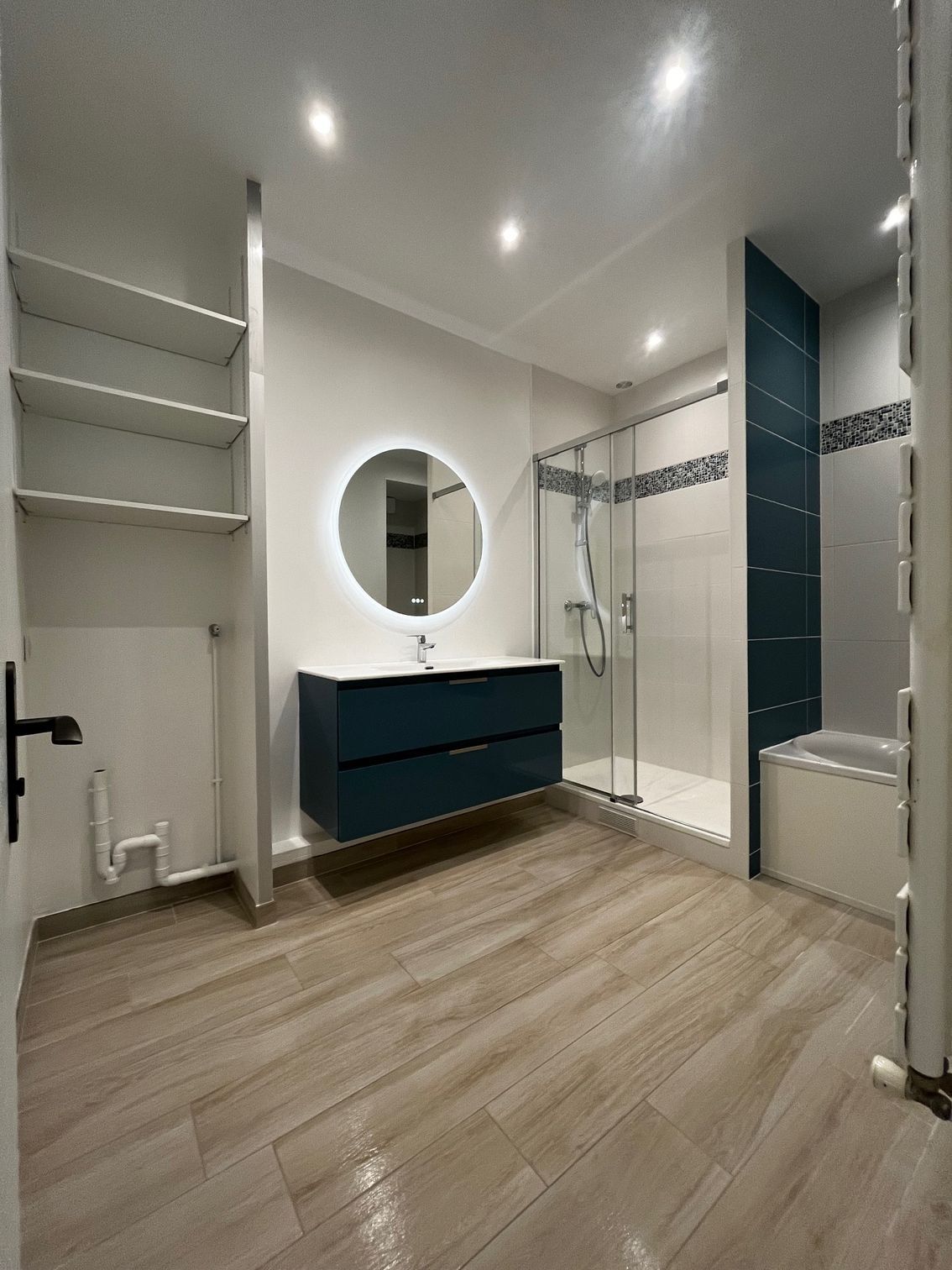 Salle de bains moderne avec parquet, lavabo, grand miroir, porte de douche et décoration blanche et noire