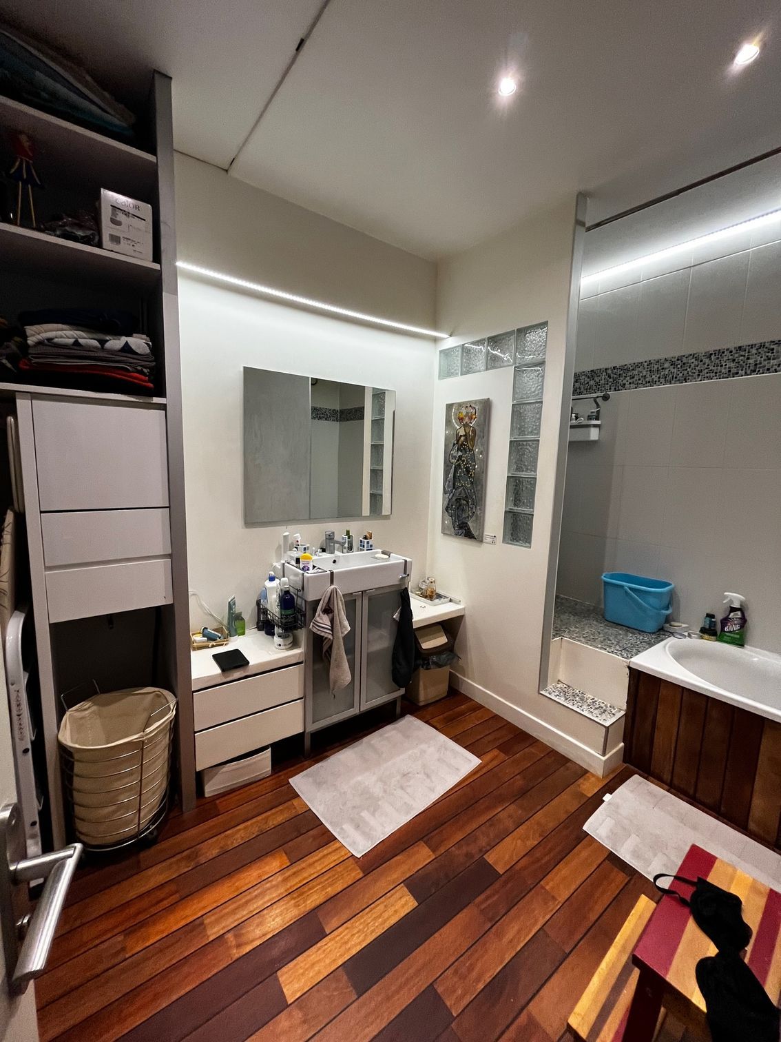 Salle de bain moderne avec meuble-lavabo, grand miroir, tapis blanc, parquet et rideau de douche