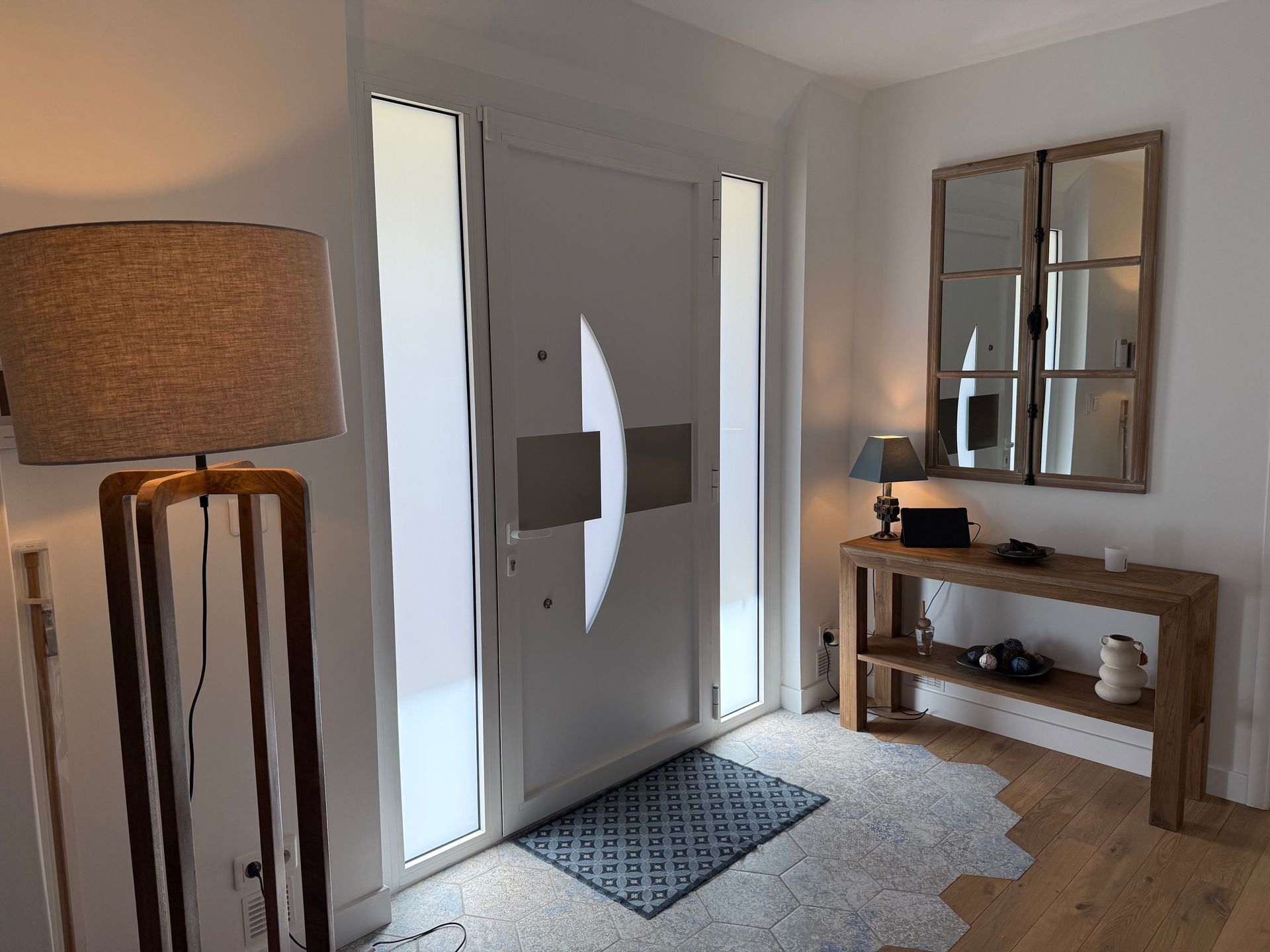 Entrée lumineuse avec double porte blanche, tapis à motifs, console en bois, miroir et lampadaire