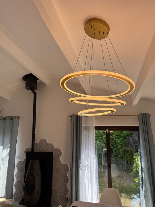 Lustre moderne à anneaux dorés circulaires suspendu à un plafond blanc dans une pièce lumineuse
