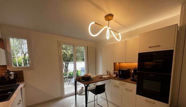 Cuisine moderne et lumineuse avec armoires blanches, tabourets d'îlot noirs et éclairage chaleureux