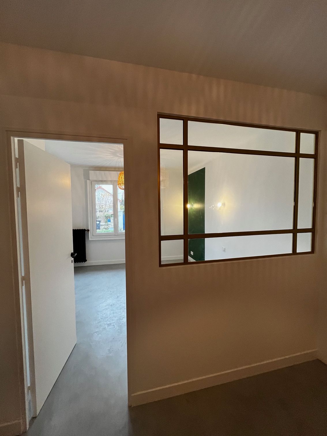 Vue du couloir donnant sur une pièce lumineuse, avec un grand miroir rectangulaire sur le mur de droite.