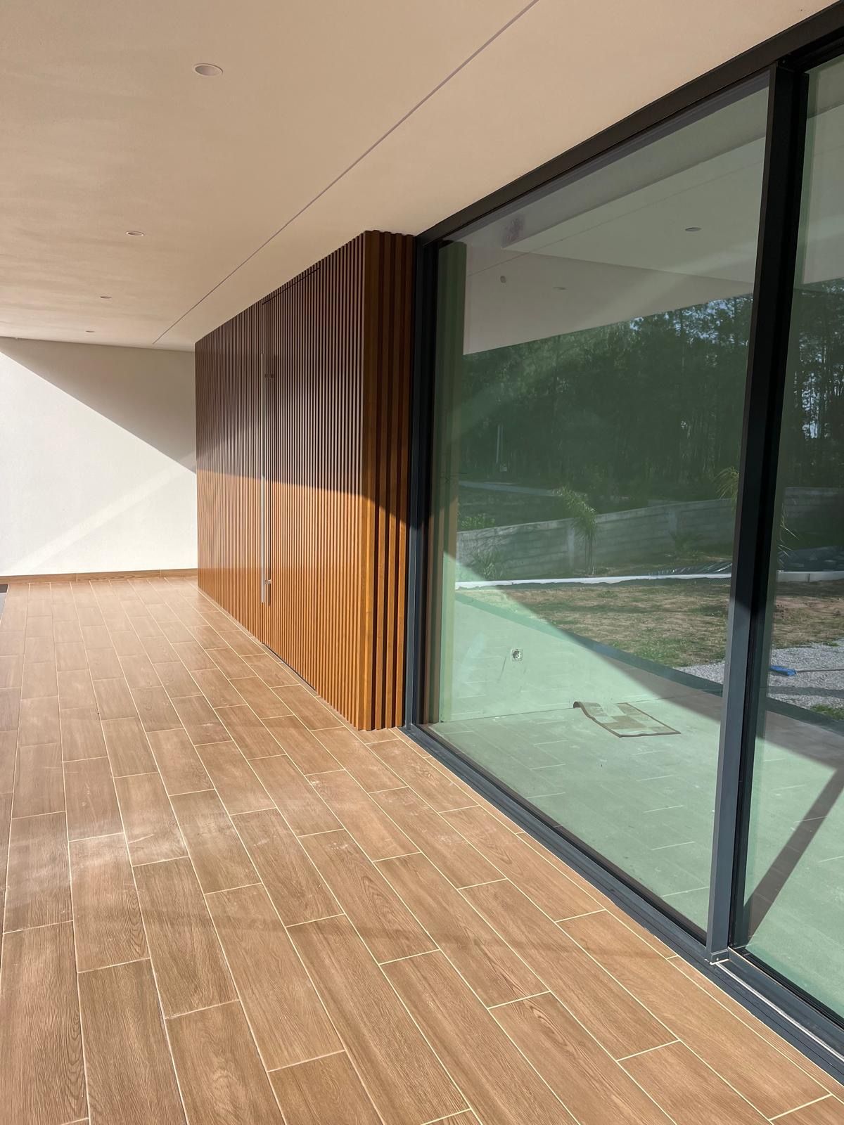 Terrasse moderne avec plancher en bois, mur à lattes verticales et grandes portes coulissantes en verre.