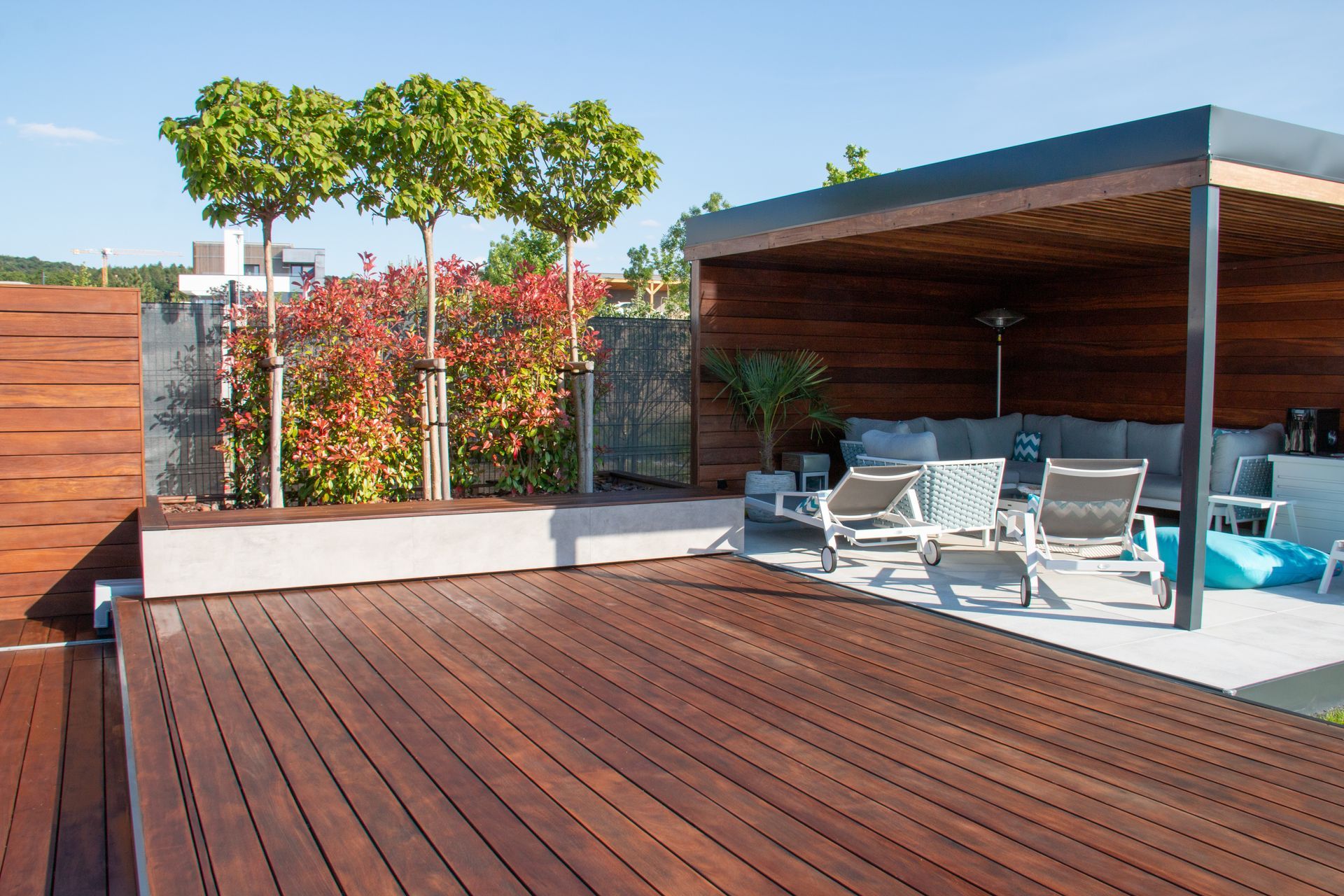 Terrasse moderne sur le toit avec plancher en bois, chaises longues, bain à remous et arbres en pot sous une pergola.