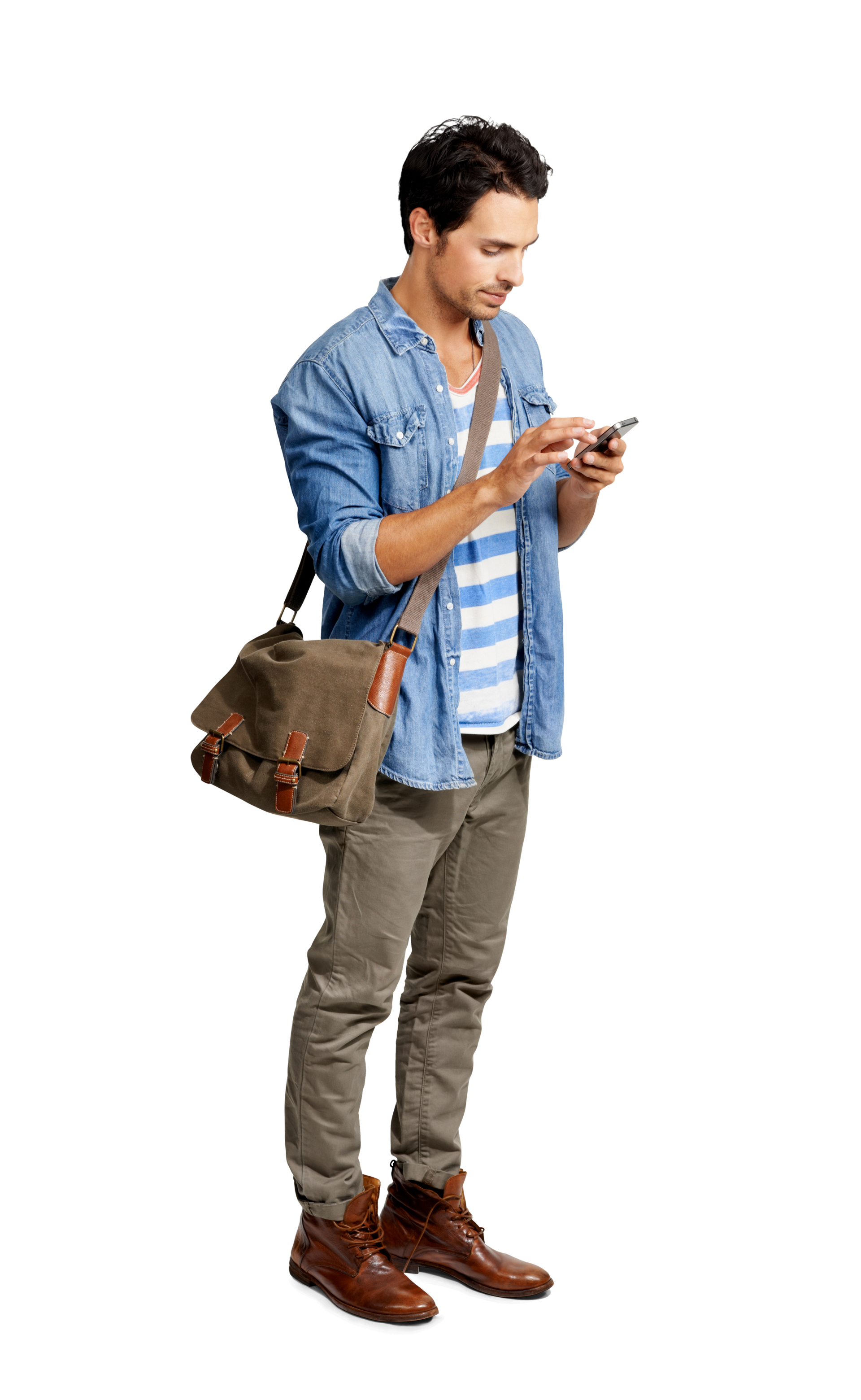 Un homme debout, regardant son téléphone, porte une chemise en jean, un pantalon, des bottes et une sacoche.