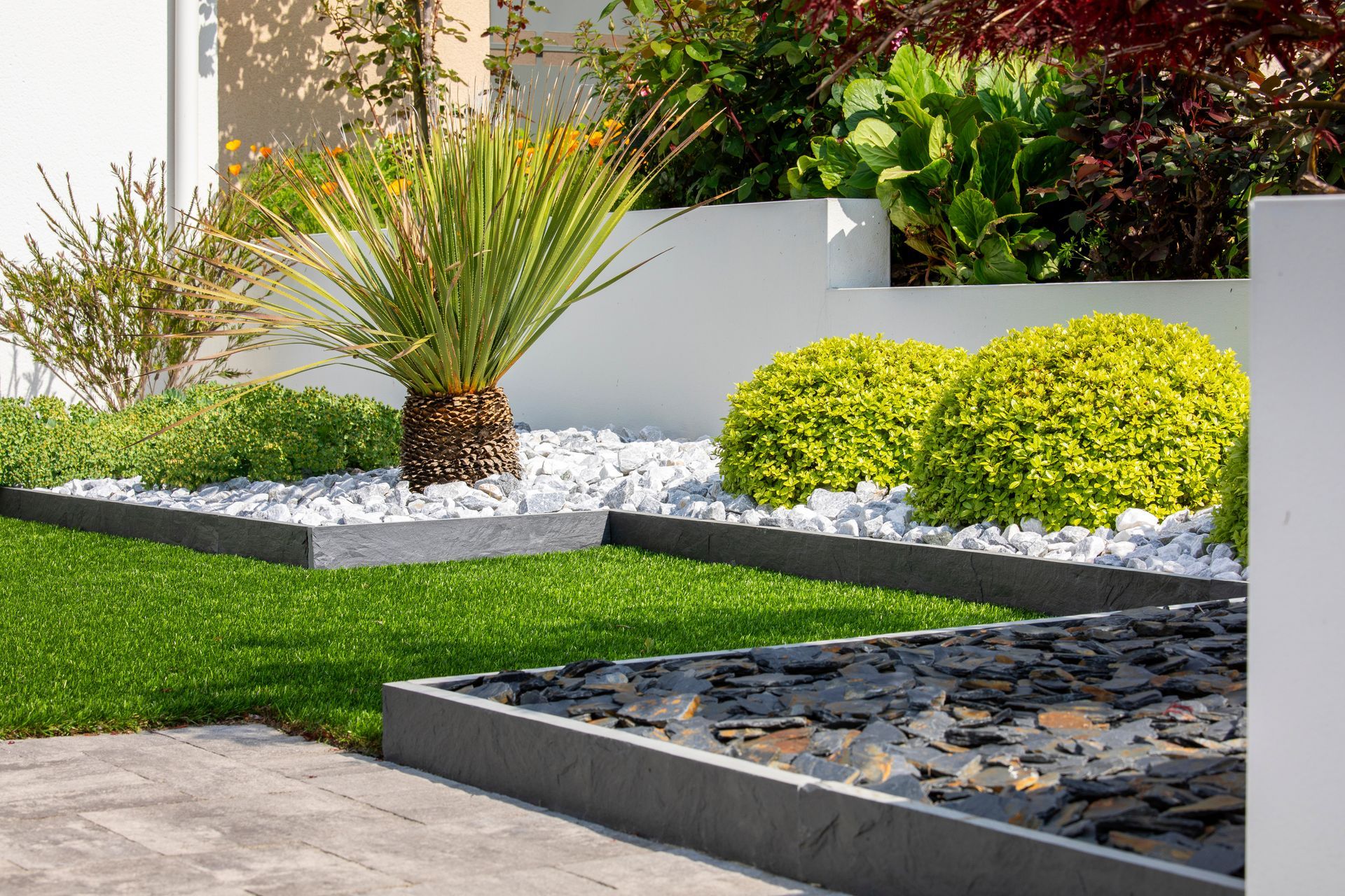 Jardin paysager moderne avec pelouse, plantes succulentes, parterres de gravier et éléments décoratifs en pierre.