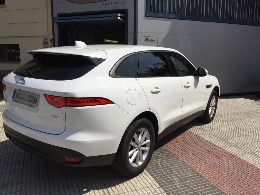 Un Jaguar F-Pace blanco está estacionado frente a un edificio.