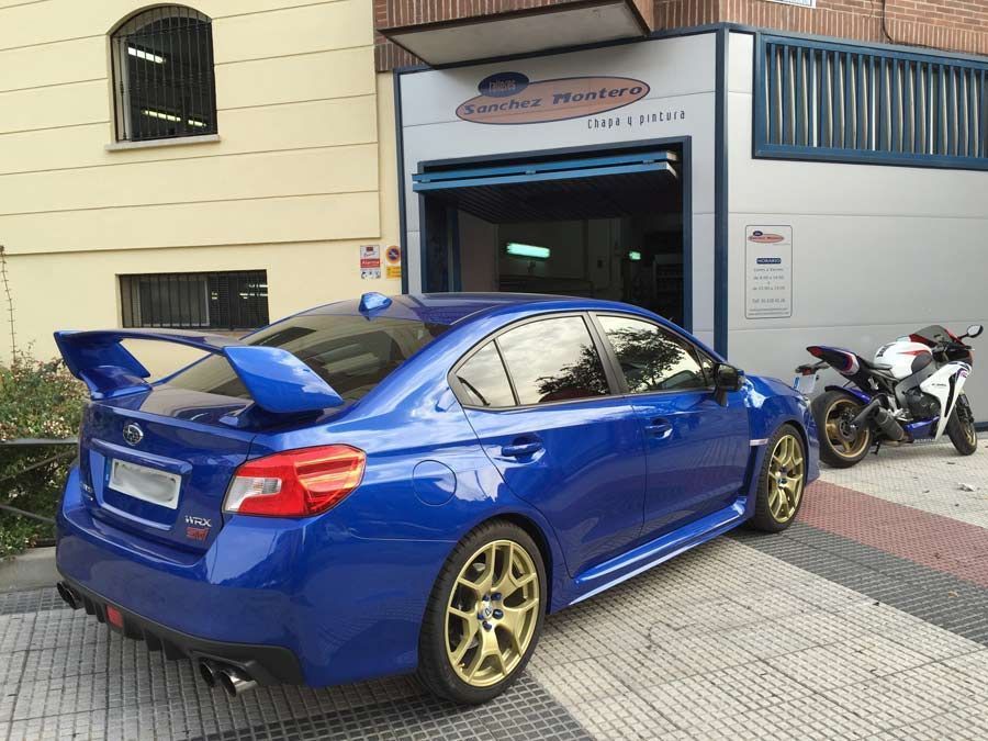 Un coche azul está aparcado delante de un edificio al lado de una motocicleta.