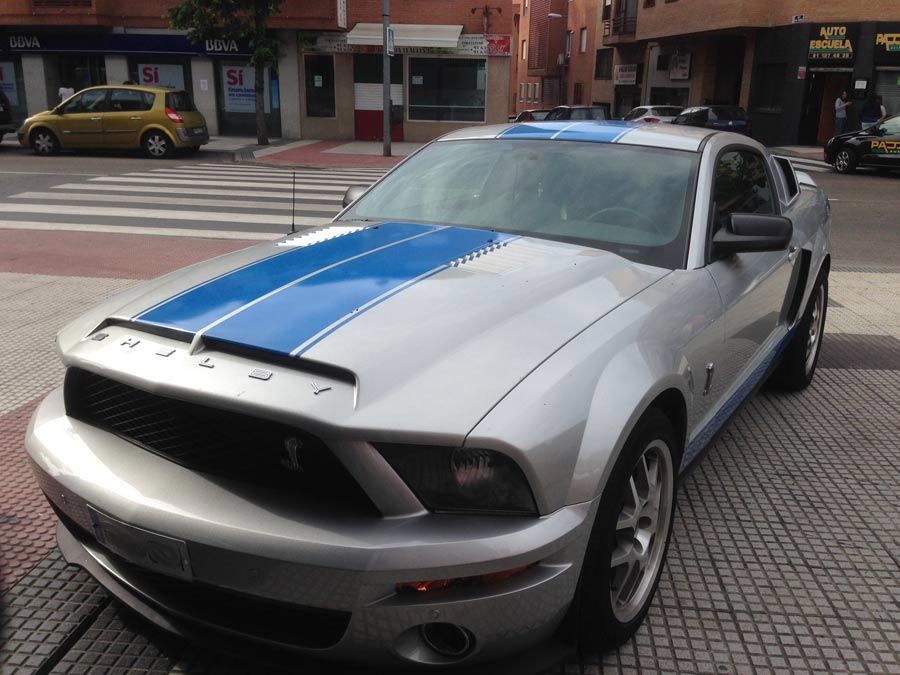 Un Mustang plateado con rayas azules en el capó.