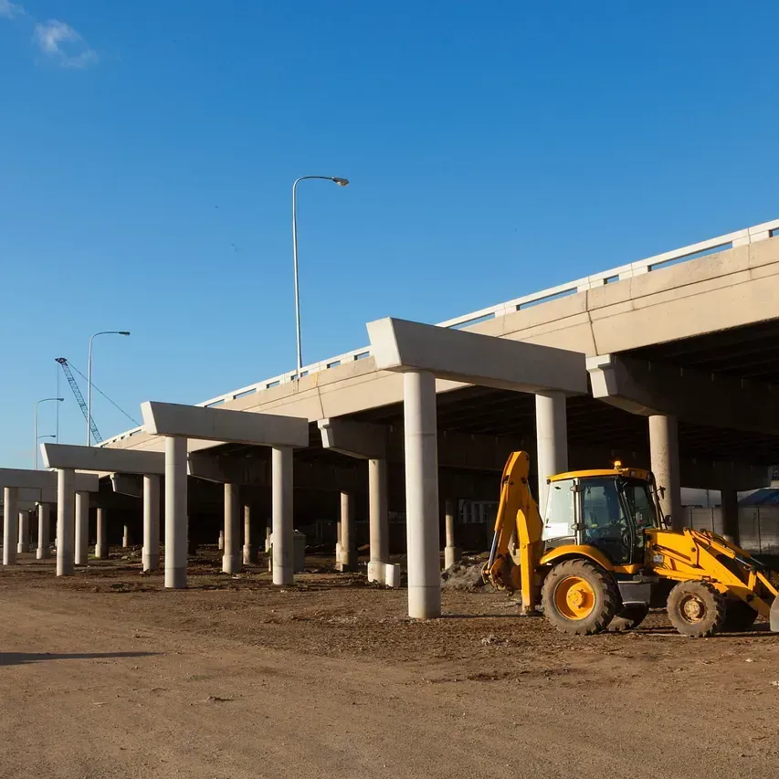 Una excavadora amarilla está estacionada debajo de un puente