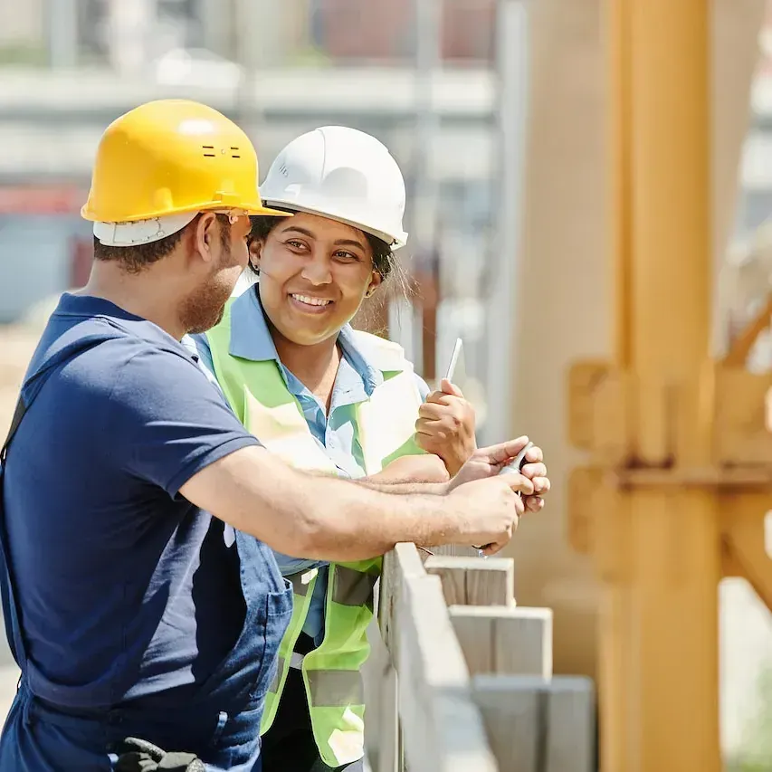 Un hombre y una mujer que llevan cascos de seguridad están hablando entre sí en un sitio de construcción.