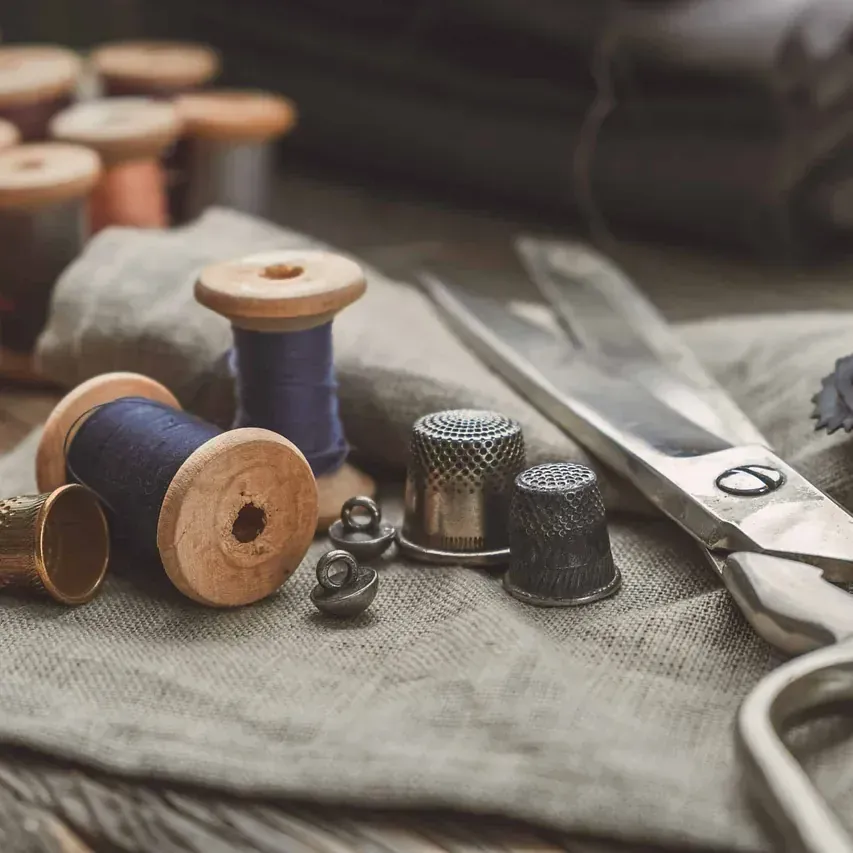 Carretes de hilo, dedales y tijeras están sobre una mesa de madera.