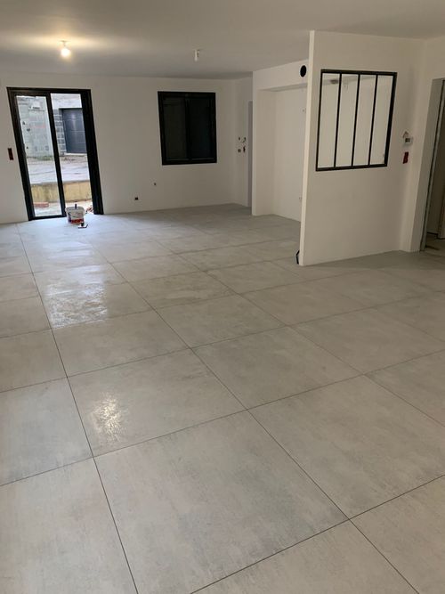 Pièce carrelée vide aux murs blancs, portes ouvertes et fenêtre laissant entrer la lumière du jour