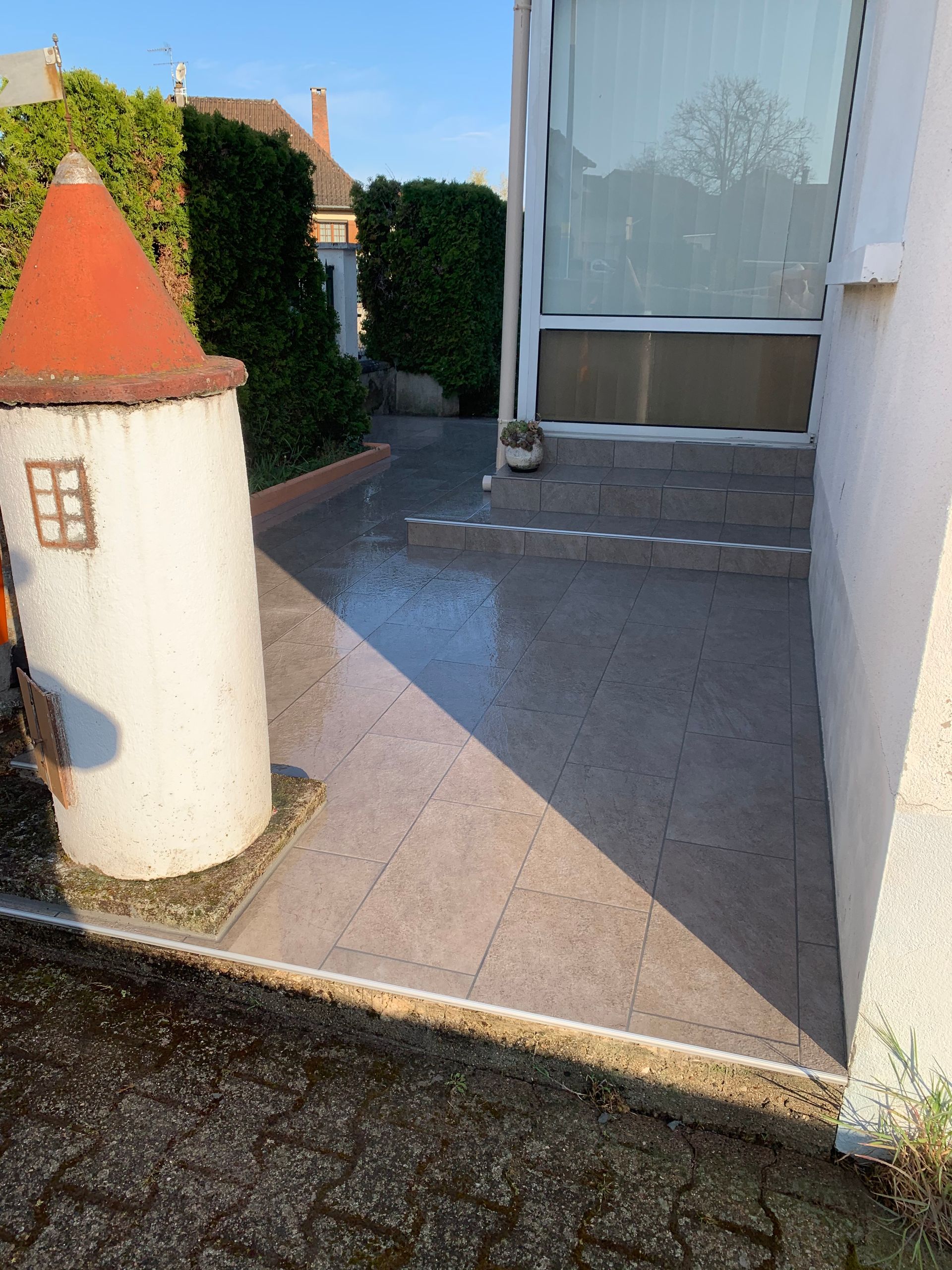 Terrasse avant avec une petite tour décorative, allée pavée et porte-fenêtre coulissante.