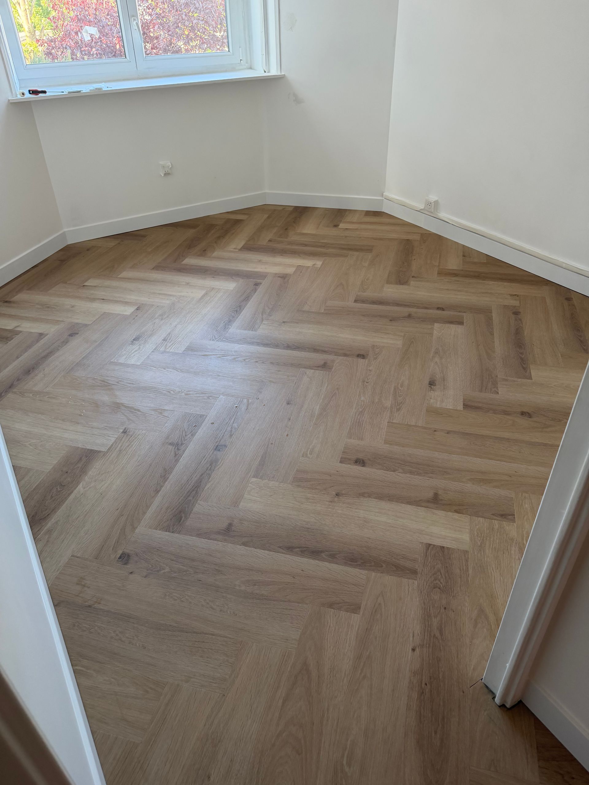 Pièce vide avec parquet clair à chevrons et une fenêtre laissant entrer la lumière du jour