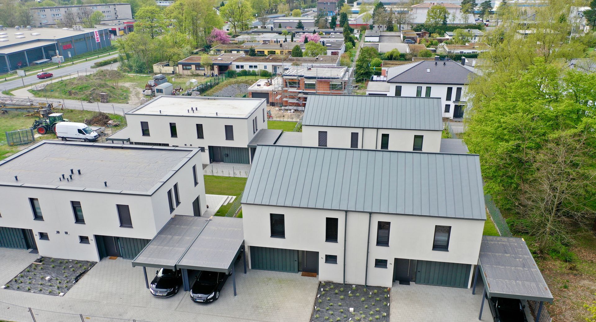 Eine Luftaufnahme von vier modernen, hellfarbigen zweistöckigen Wohngebäuden mit grauen Dächern und angebauten Carports.