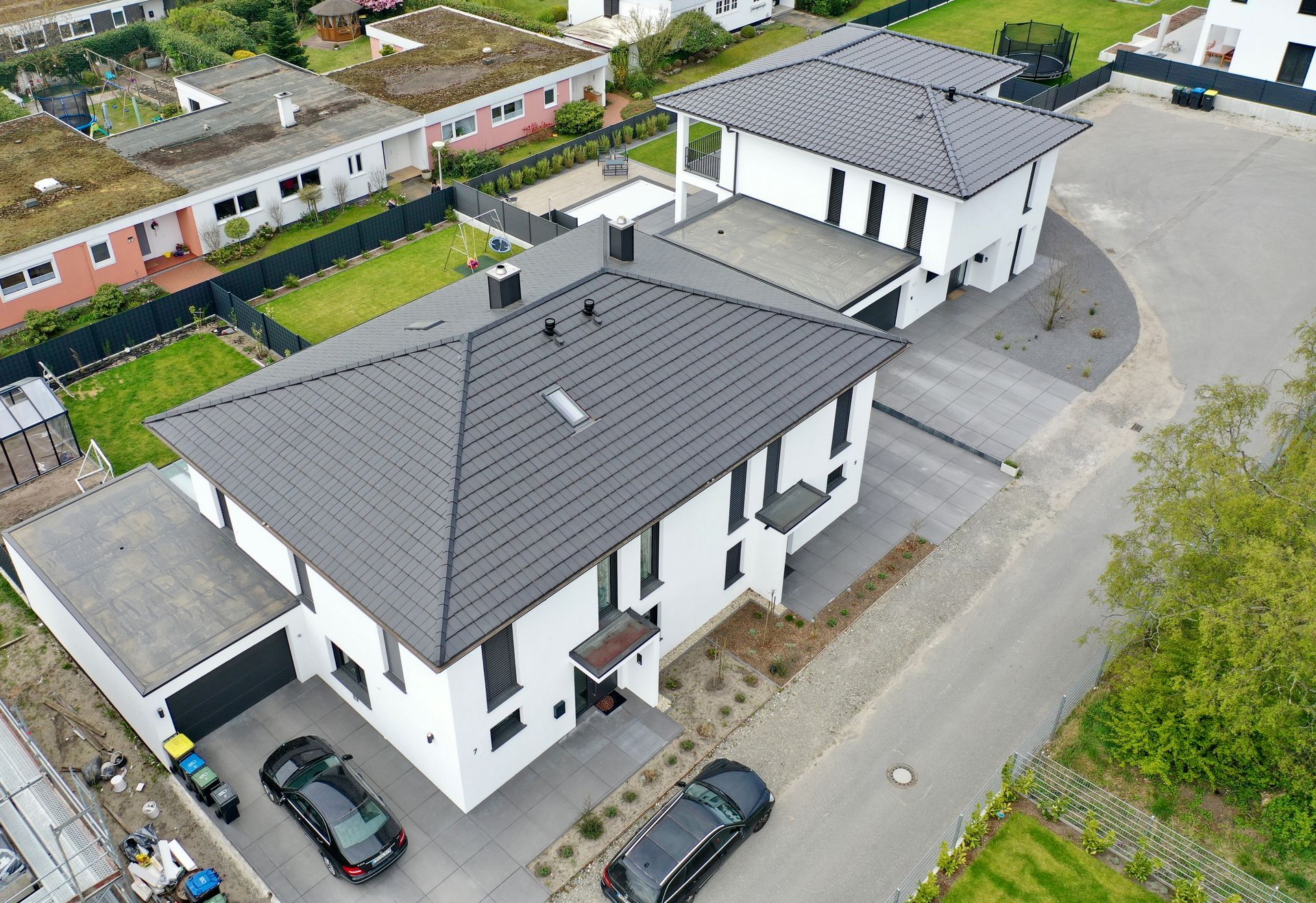 Luftaufnahme von zwei modernen weißen Häusern mit grauen Ziegeldächern und angebauten Garagen in einem Vorstadtgebiet.