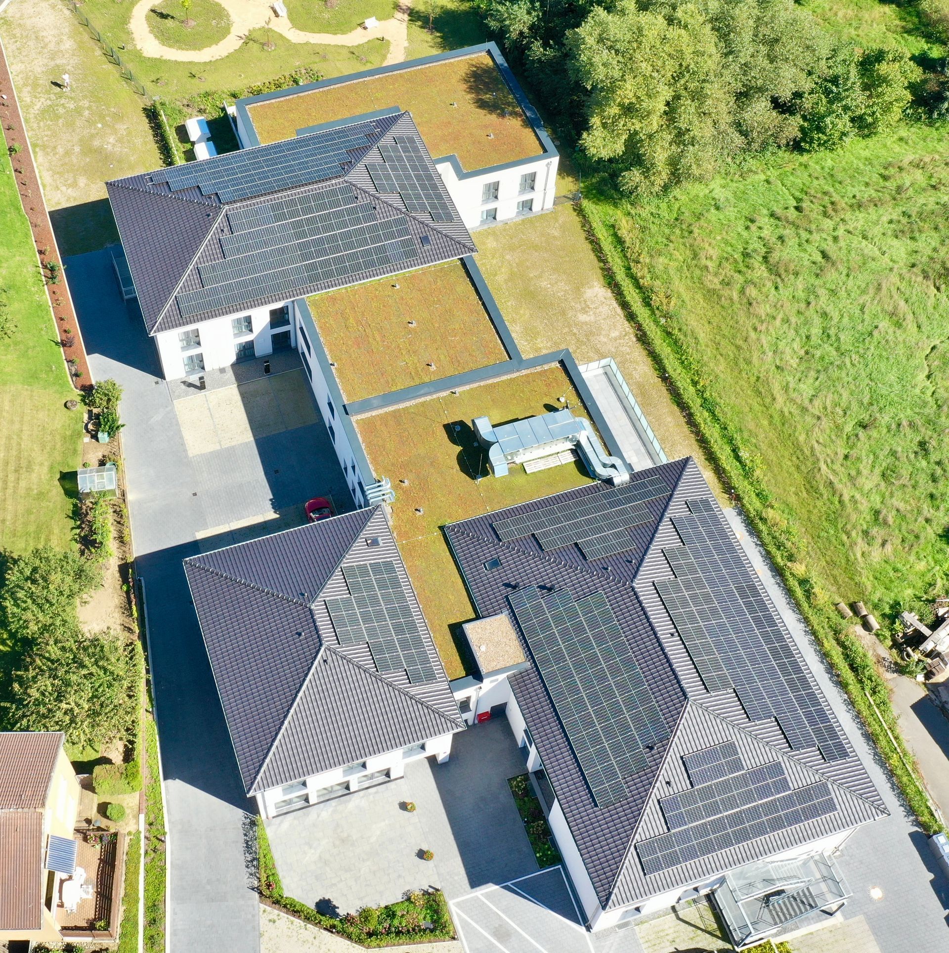 Eine Luftaufnahme eines mehrteiligen Gebäudes mit dunklen Schindeldächern, grünen Flachdächern und gepflasterten Innenhöfen.