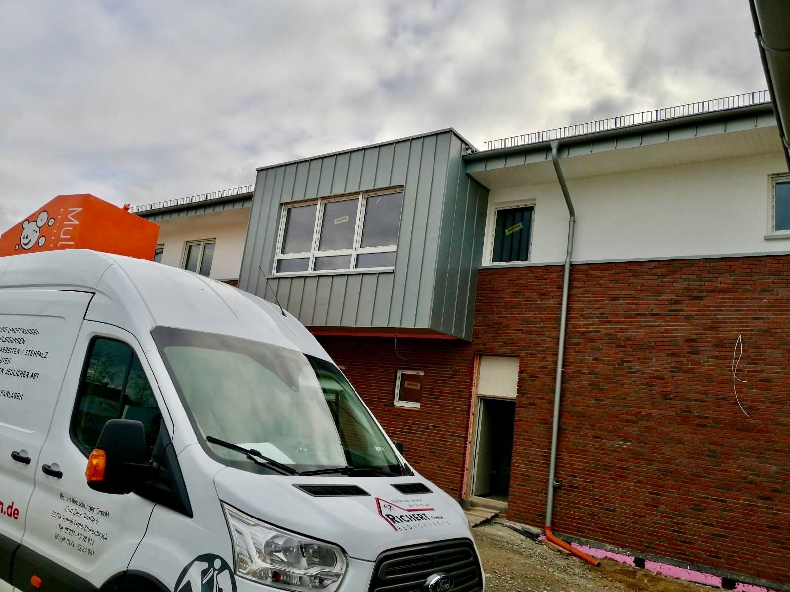 Modernes Backsteingebäude mit einem metallverkleideten Fensterabschnitt im Obergeschoss.