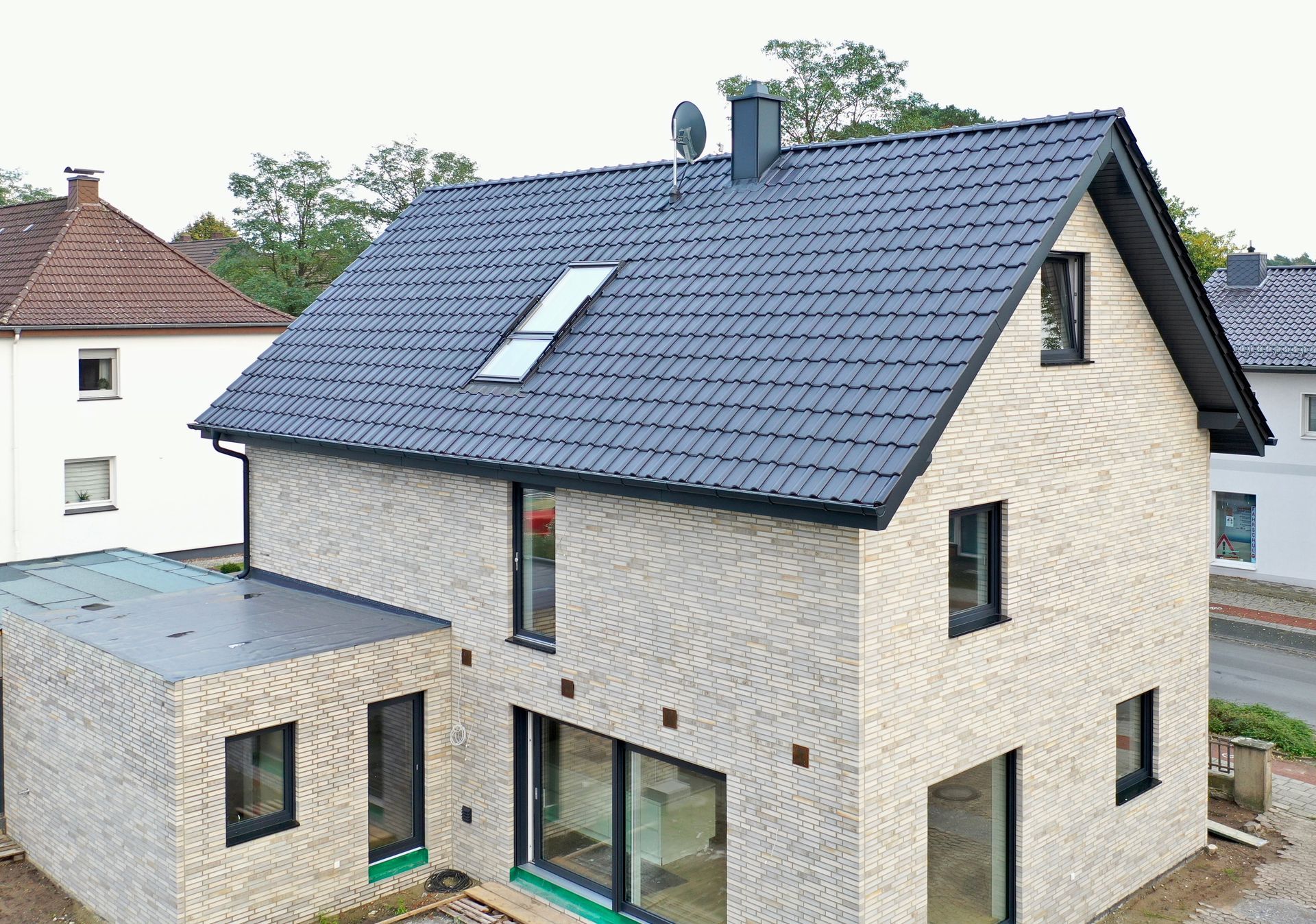 Ein zweistöckiges Haus mit heller Backsteinfassade, dunklem Satteldach und großen Fenstern