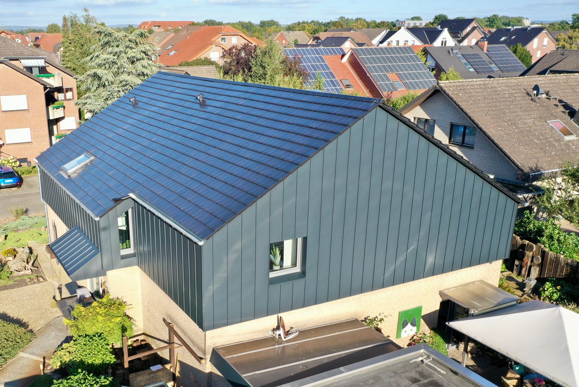 Luftaufnahme eines Hauses mit modernem blaugrauem Metalldach und dazu passender vertikaler Schindelfassade