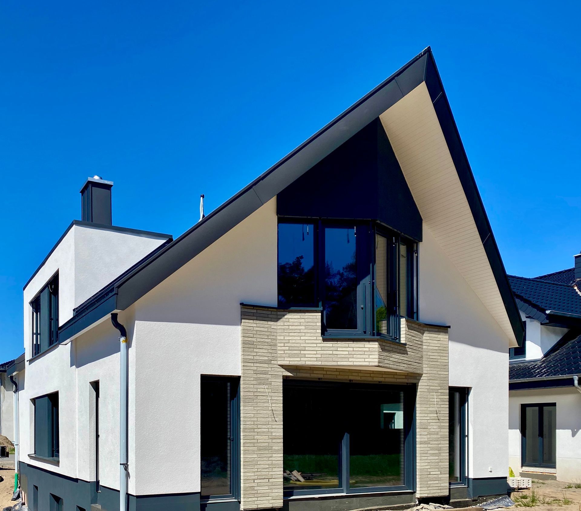 Modernes zweistöckiges Haus mit steilem Giebeldach, weißen Stuckwänden, Steinelementen und dunklen Fensterrahmen