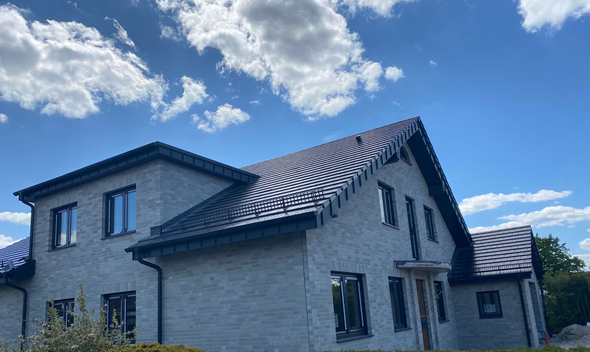 Ein zweistöckiges, hellgraues Backsteinhaus mit dunklem Dach und dunklen Fensterrahmen