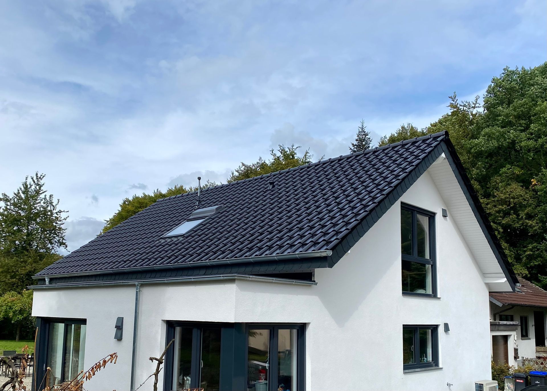 Ein modernes zweistöckiges Haus mit weißen Außenwänden, dunkelgrauen Fensterrahmen und einem dunklen Ziegeldach