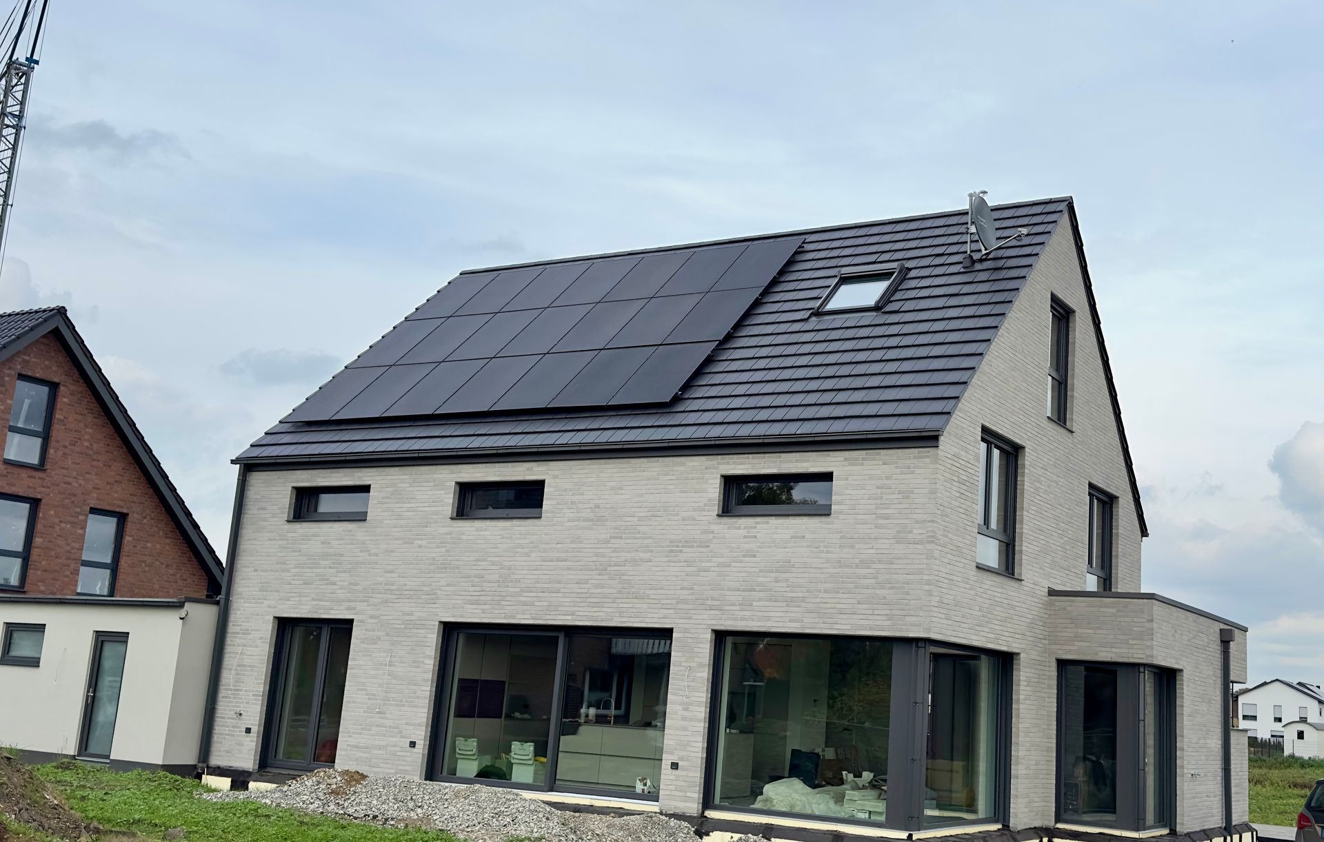 Ein zweistöckiges, modernes, hellfarbiges Backsteinhaus mit dunklen Solarpaneelen auf dem Dach und großen Glasfenstern.