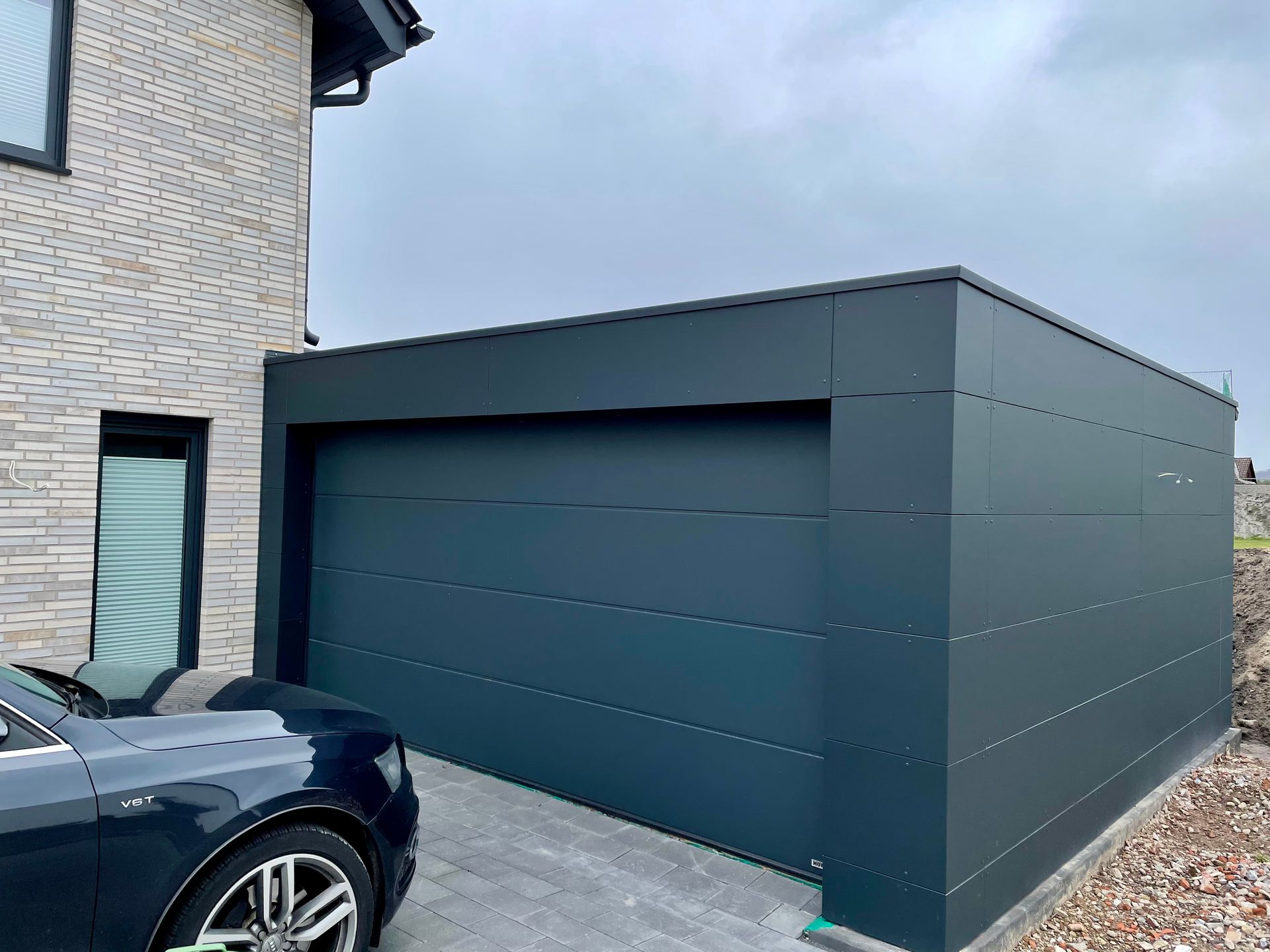 Eine moderne, dunkelgraue Garagenfassade, die an ein mit Stein verkleidetes Haus angebaut ist